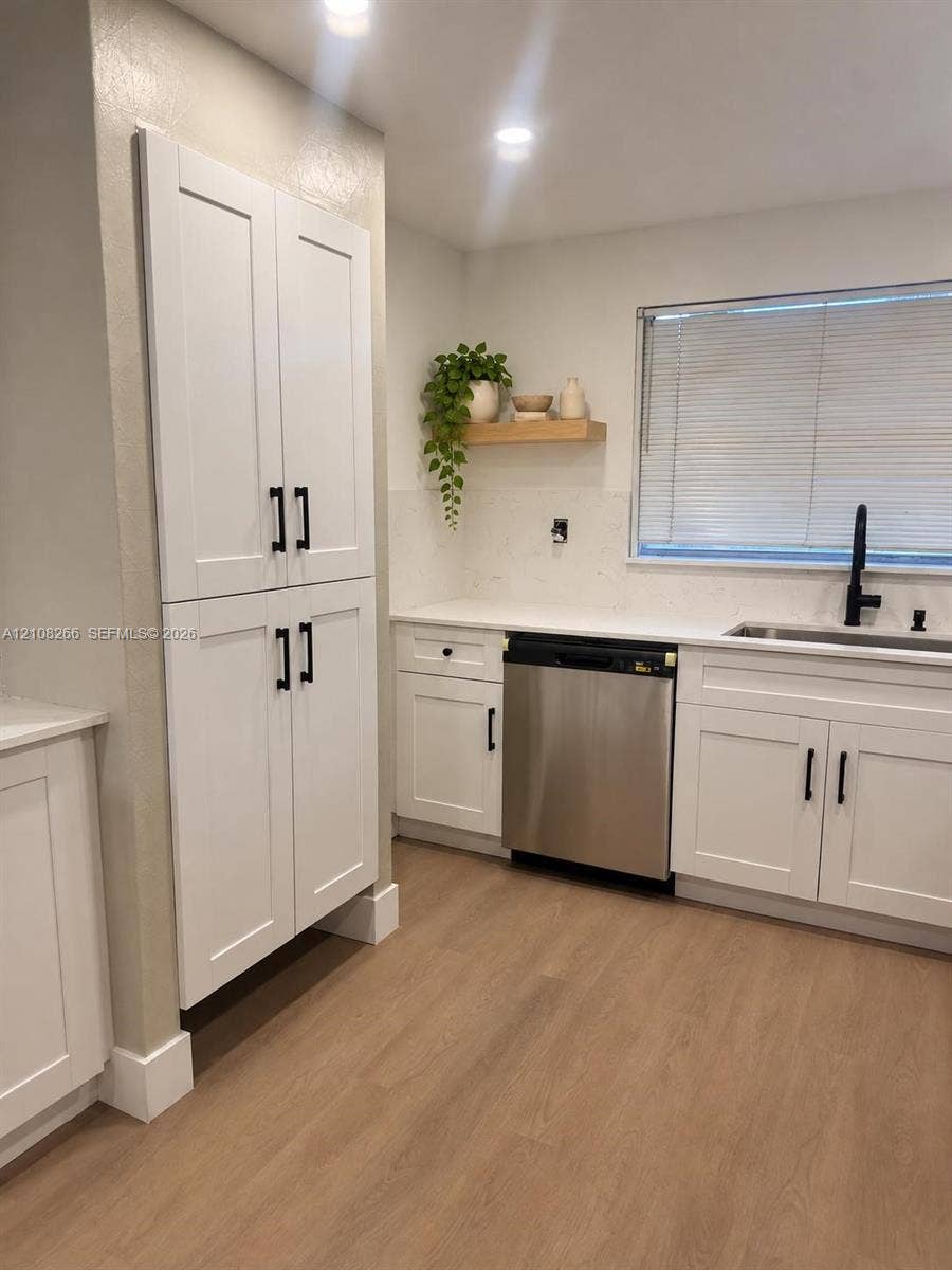 9721 Sunrise Lakes Boulevard, #108, Sunrise, FL 33322 White Shaker-style cabinetry featuring matte black hardware, stone-finish countertops, stainless steel dishwasher, undermount sink with a matte black faucet, and wood-finish flooring