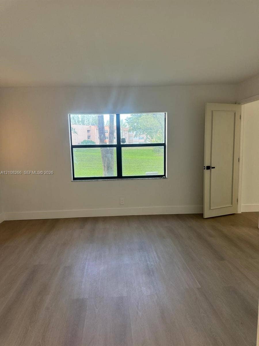 9721 Sunrise Lakes Boulevard, #108, Sunrise, FL 33322 Interior room featuring light-toned wood-finish flooring, a single-pane window with black framing, and a white recessed-panel door with matte black hardware