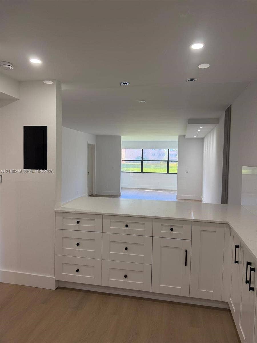 9721 Sunrise Lakes Boulevard, #108, Sunrise, FL 33322 Kitchen featuring white cabinetry with matte black hardware, stone-finish countertops, recessed lighting, and wood-finish flooring