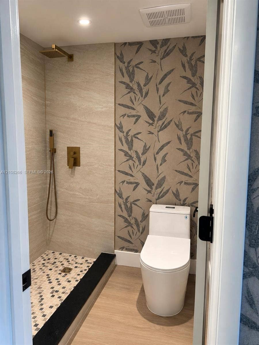 9721 Sunrise Lakes Boulevard, #108, Sunrise, FL 33322 Walk-in shower with stone-finish tile surround, gold-tone hardware, multi-colored mosaic tile flooring, and contrasting black threshold