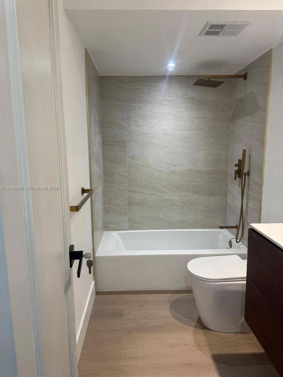 9721 Sunrise Lakes Boulevard, #108, Sunrise, FL 33322 Bathroom featuring a soaking tub, floor-to-ceiling tile surround, metallic finish shower fixtures with handheld sprayer, wood-finish vanity, and wood-finish flooring
