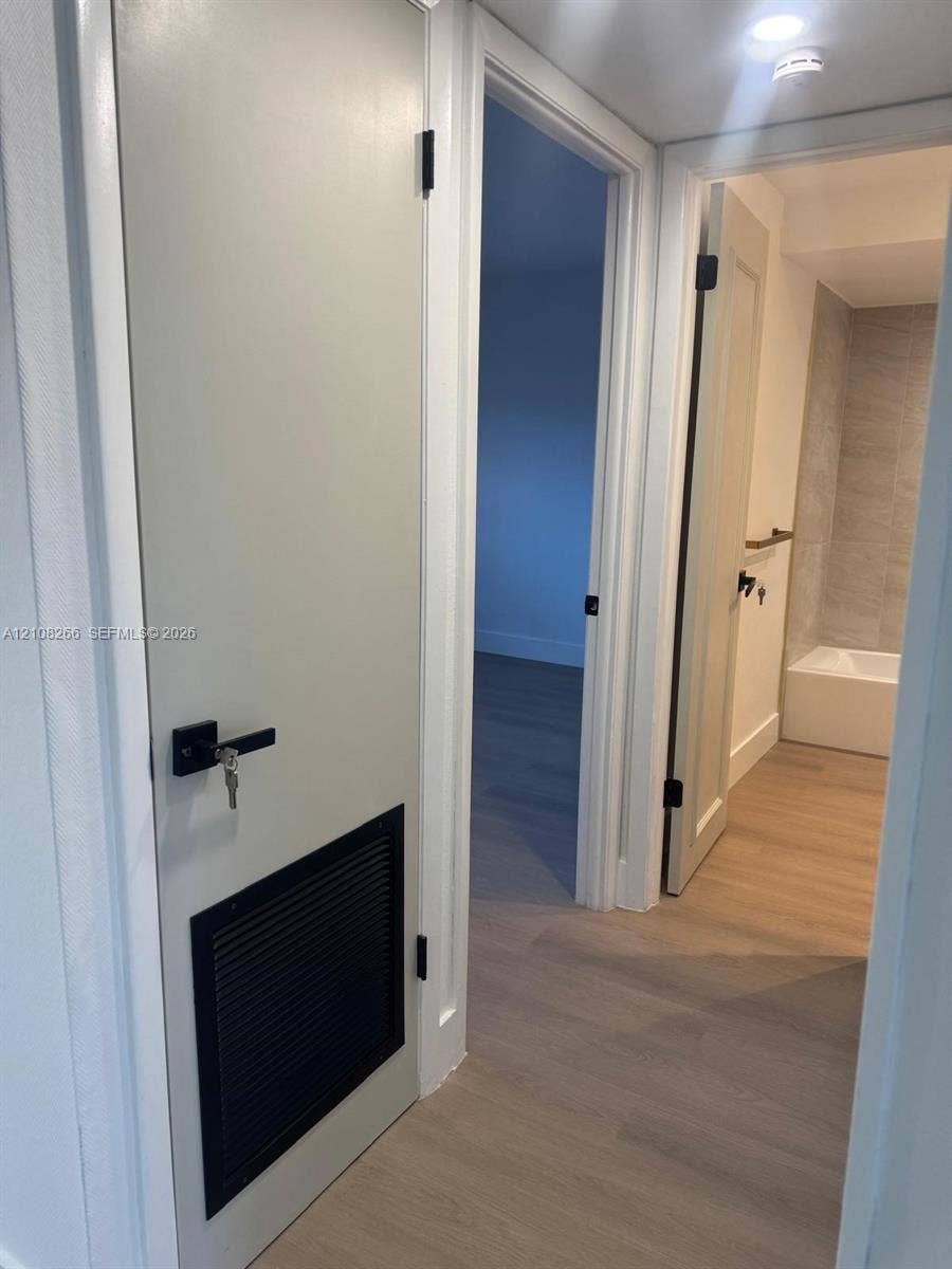 9721 Sunrise Lakes Boulevard, #108, Sunrise, FL 33322 Interior hallway featuring wood-finish flooring, white doors with matte black hardware, and an integrated black door ventilation grille