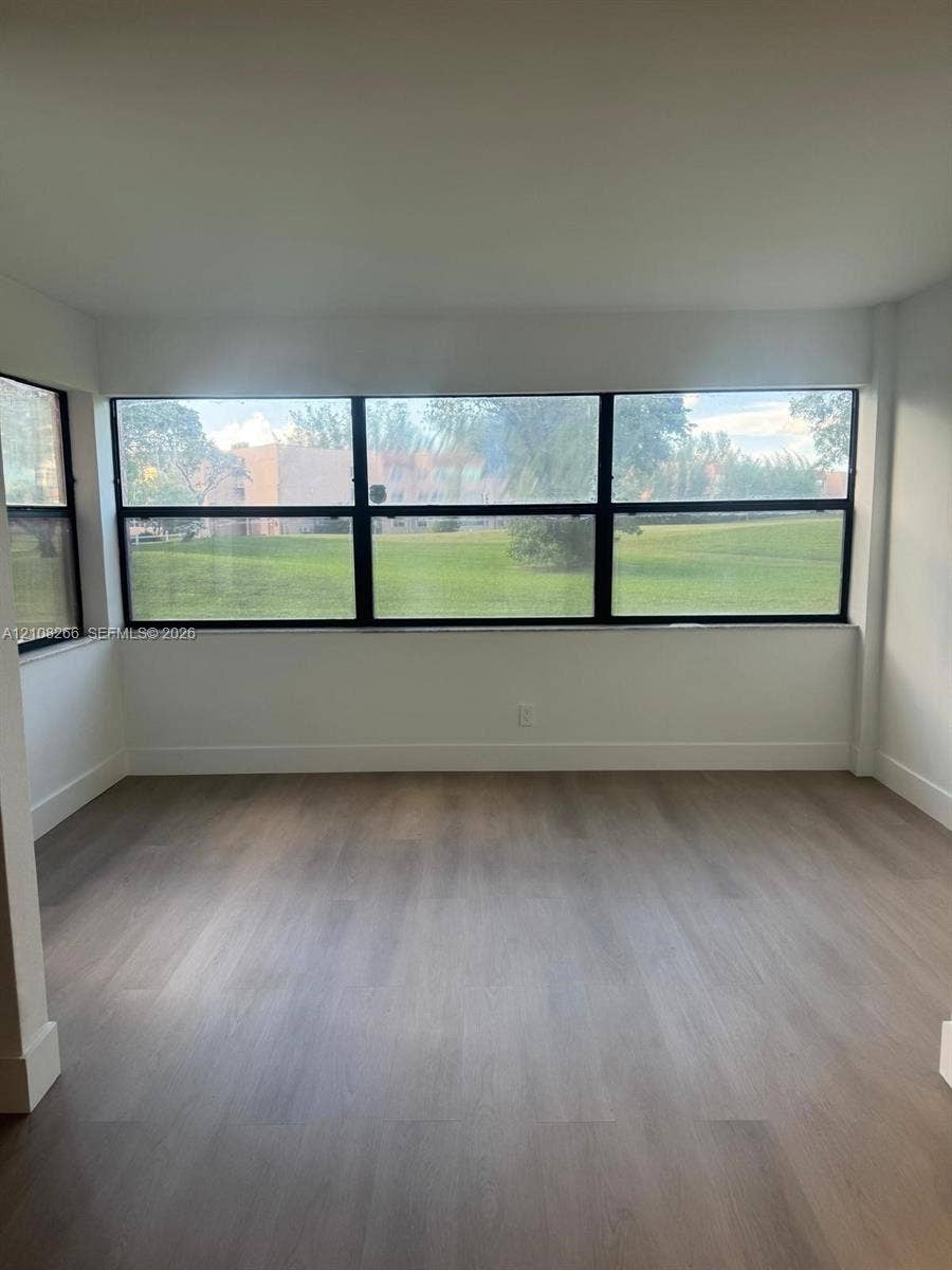 9721 Sunrise Lakes Boulevard, #108, Sunrise, FL 33322 Interior space featuring wood-finish flooring, neutral walls, and floor-to-ceiling windows with dark framing