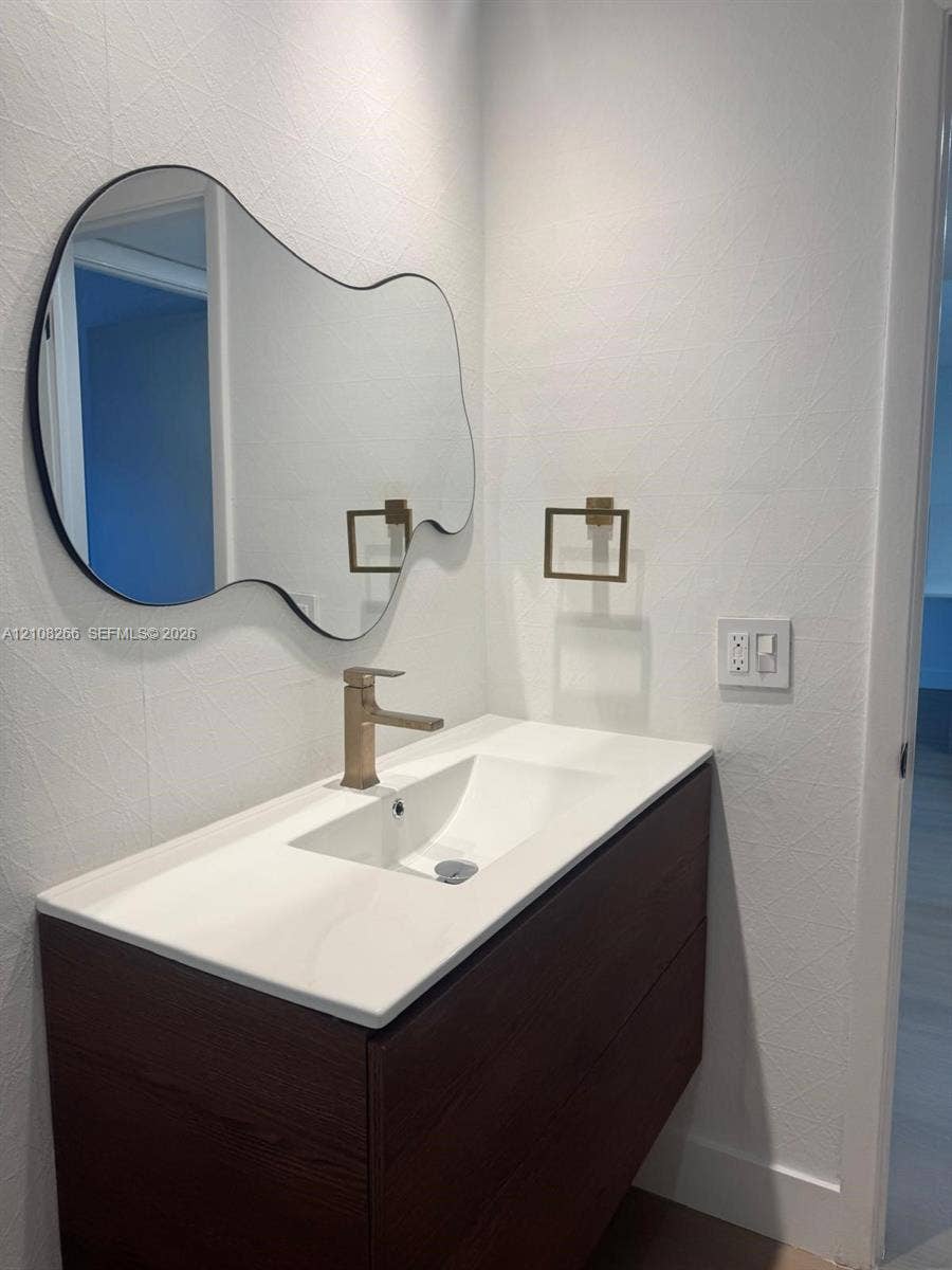 9721 Sunrise Lakes Boulevard, #108, Sunrise, FL 33322 Floating vanity with dark wood-finish cabinetry, white countertop, integrated sink, metallic finish faucet, and organic-shaped mirror