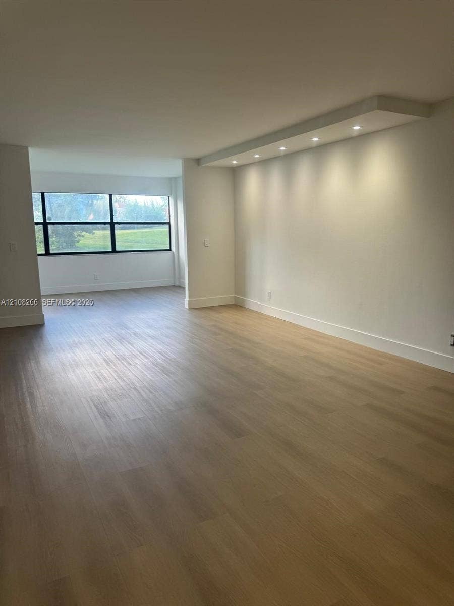 9721 Sunrise Lakes Boulevard, #108, Sunrise, FL 33322 Open-concept interior featuring light wood-finish flooring, a recessed soffit with integrated downlighting, and large-format multi-pane windows
