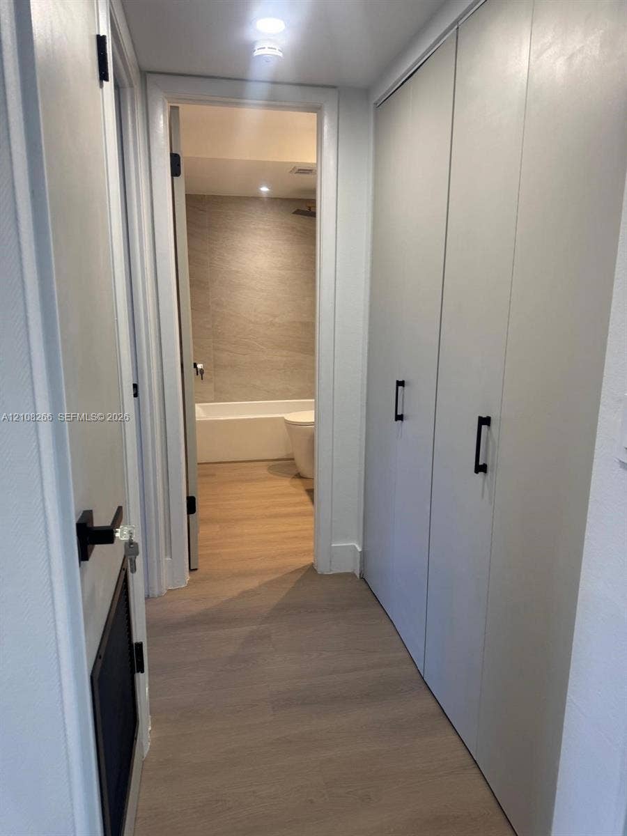 9721 Sunrise Lakes Boulevard, #108, Sunrise, FL 33322 Hallway featuring floor-to-ceiling built-in cabinetry with matte black hardware, wood-finish flooring, recessed lighting, and access to a bathroom with a tiled wall surround and tub