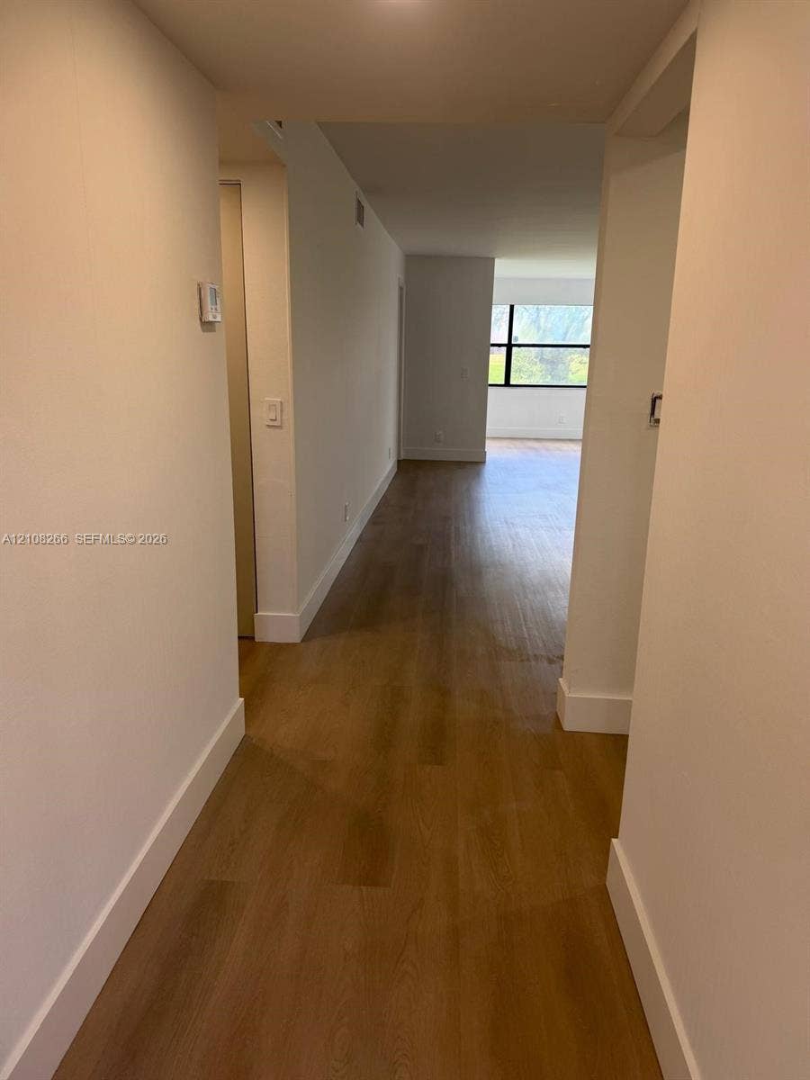 9721 Sunrise Lakes Boulevard, #108, Sunrise, FL 33322 Interior corridor featuring wood-finish flooring, neutral walls, and a multi-pane window