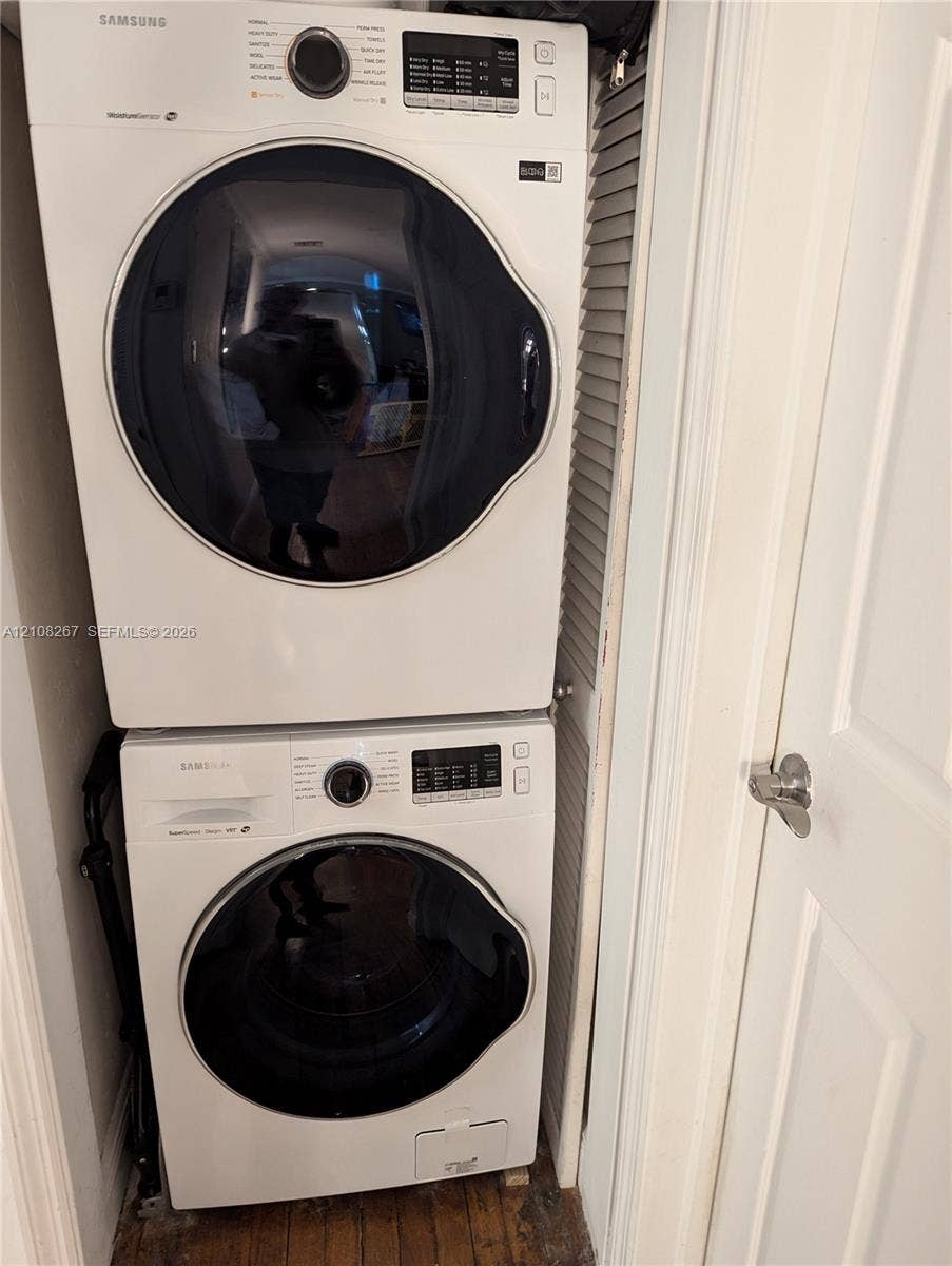 Stacked white front-load washer and dryer unit, louvered closet door, and interior door with brushed nickel hardware