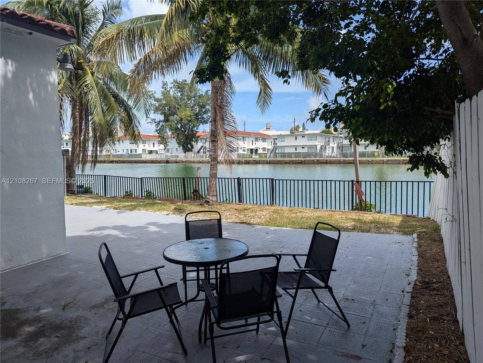 Concrete patio with metal fencing overlooking a canal, mature palm trees, and a white privacy fence