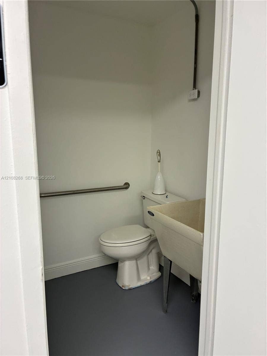 Restroom featuring an integrated utility sink, two-piece toilet, stainless steel grab bar, and resilient dark-tone flooring