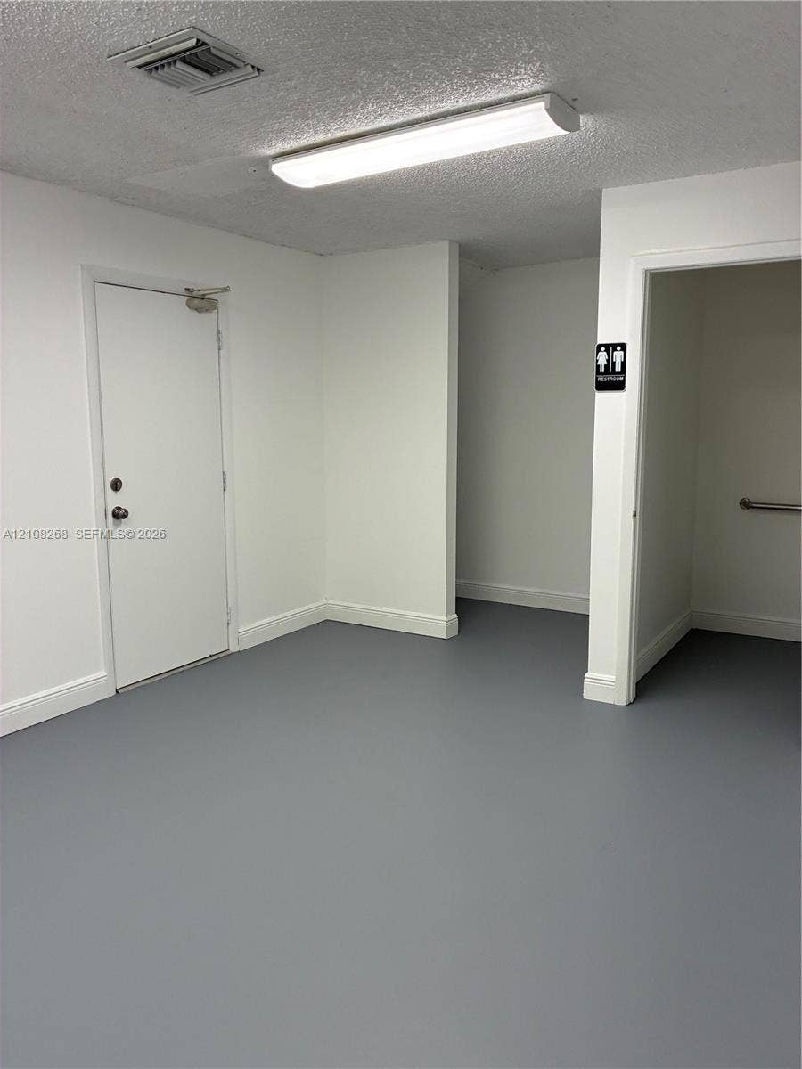Neutral-toned interior space featuring solid-surface flooring, flush-mount lighting, and a metal-clad entry door