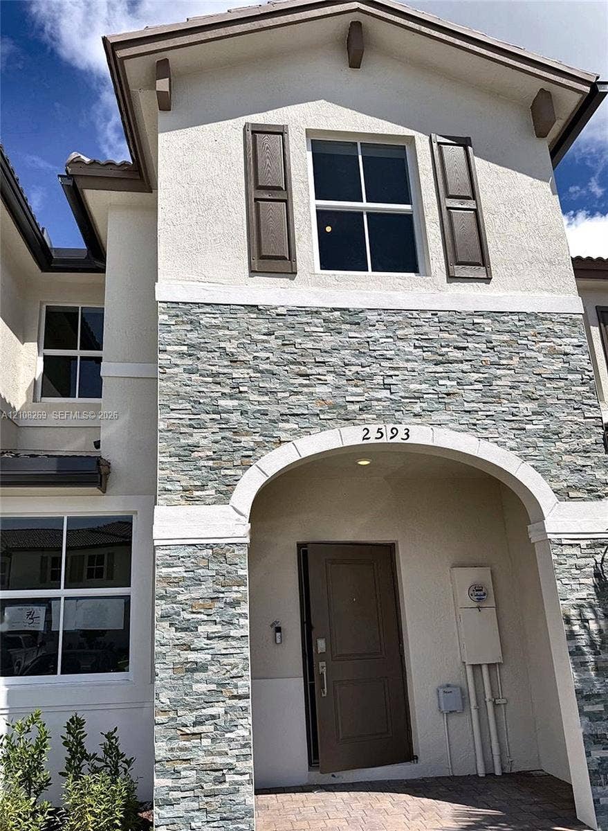 2593 SE 25th Drive, Homestead, Homestead, FL 33035 Exterior facade featuring a combination of stucco and stone veneer, arched entryway, dark-finish shutters, and multi-pane windows