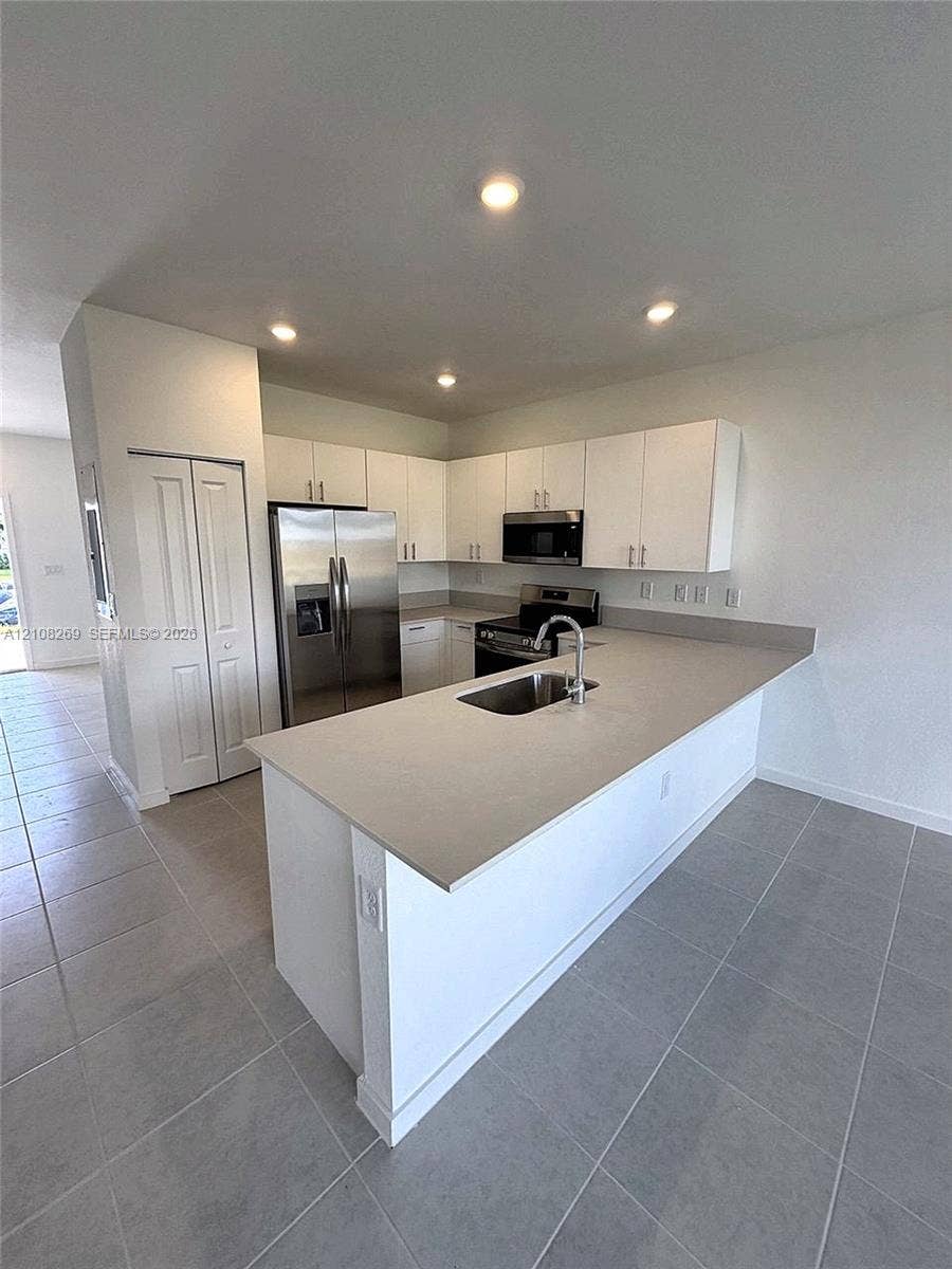 2593 SE 25th Drive, Homestead, Homestead, FL 33035 Kitchen featuring white flat-panel cabinetry, a peninsula with a stainless steel sink, quartz countertops, recessed lighting, and large-format tile flooring
