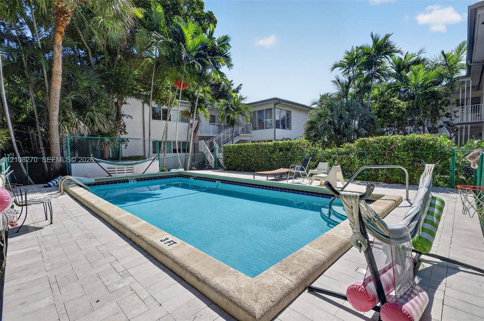 1125 99th Street, #12, Bay Harbor Islands, FL 33154 Swimming pool with concrete coping, surrounded by stone-paver decking, mature palm trees, and perimeter privacy hedging