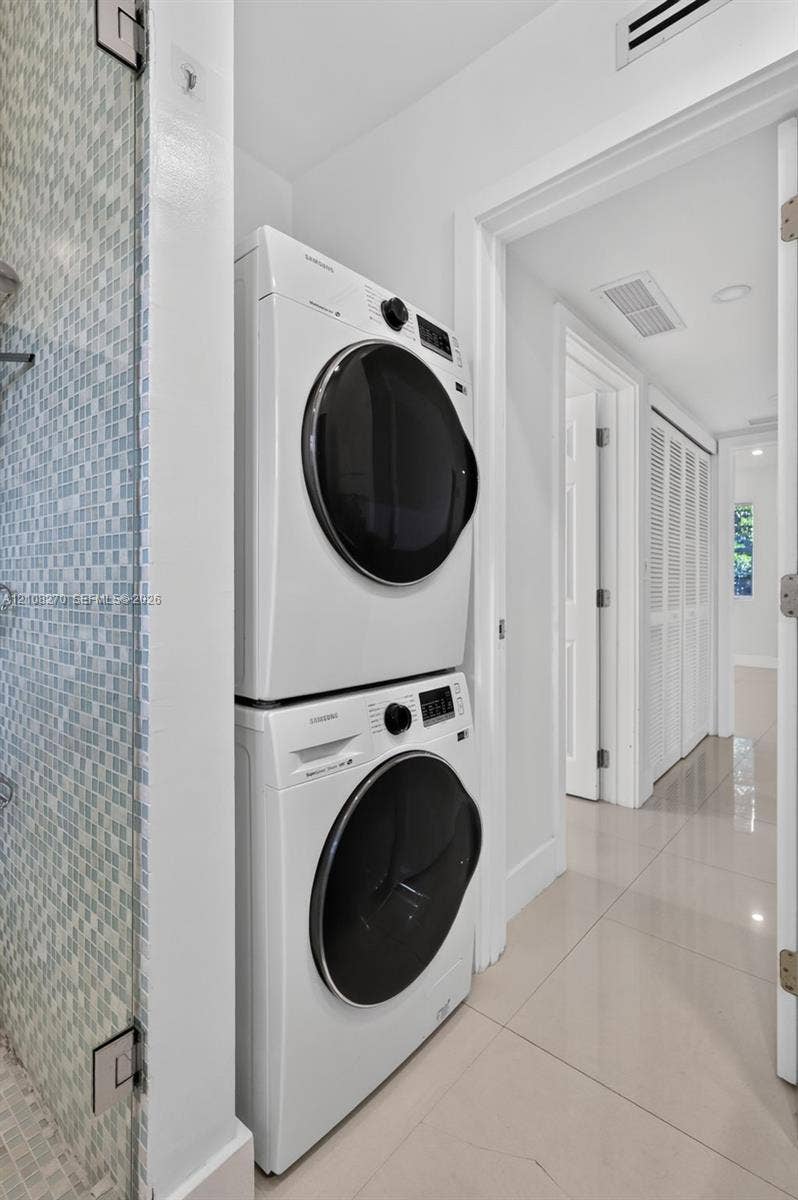 1125 99th Street, #12, Bay Harbor Islands, FL 33154 Laundry area featuring a stacked washer and dryer unit, glass-enclosed shower with mosaic wall tile, and large-format tile flooring
