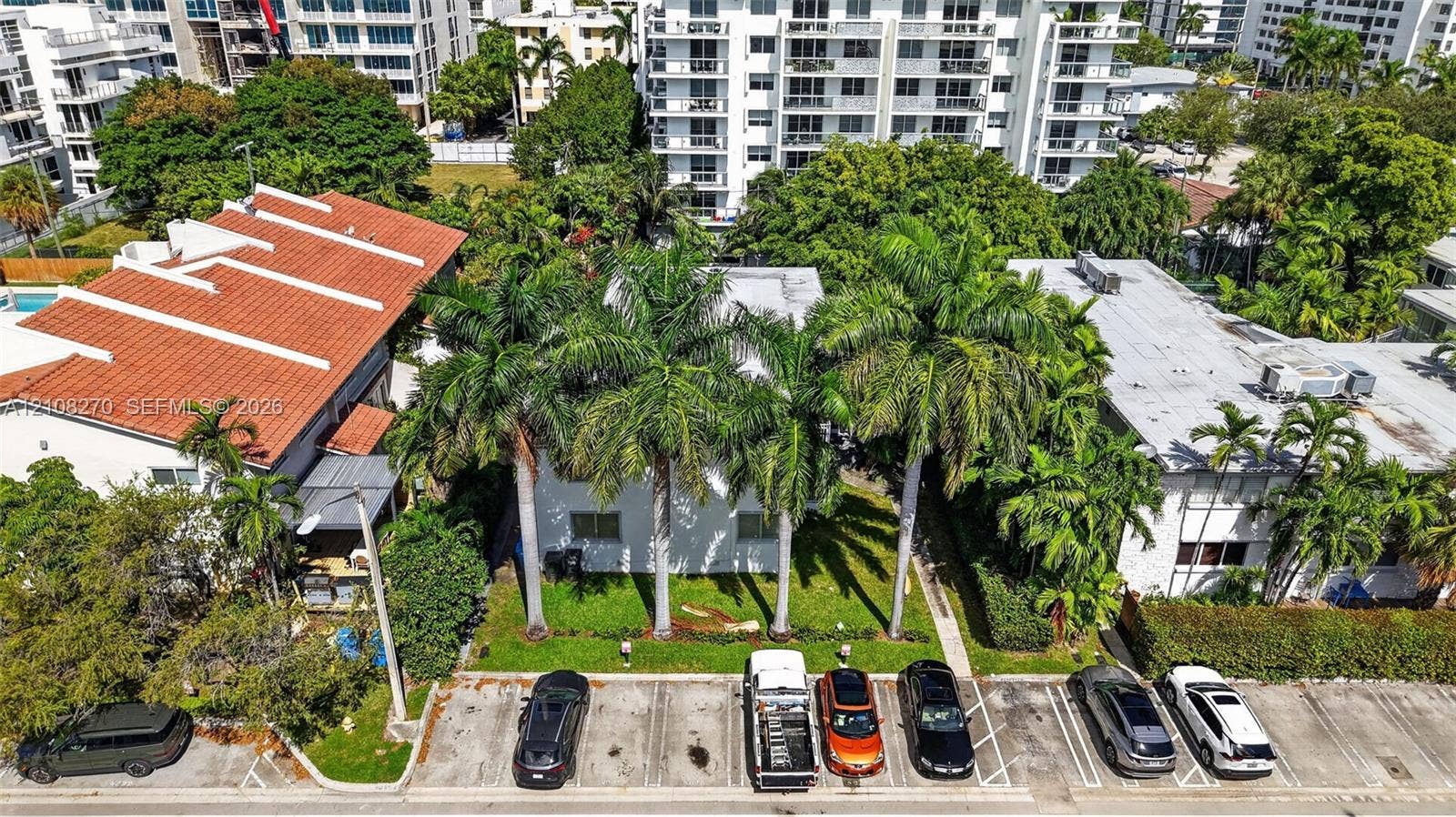 1125 99th Street, #12, Bay Harbor Islands, FL 33154 Aerial perspective featuring a multi-story building with a flat roof, mature palm trees, and designated surface parking