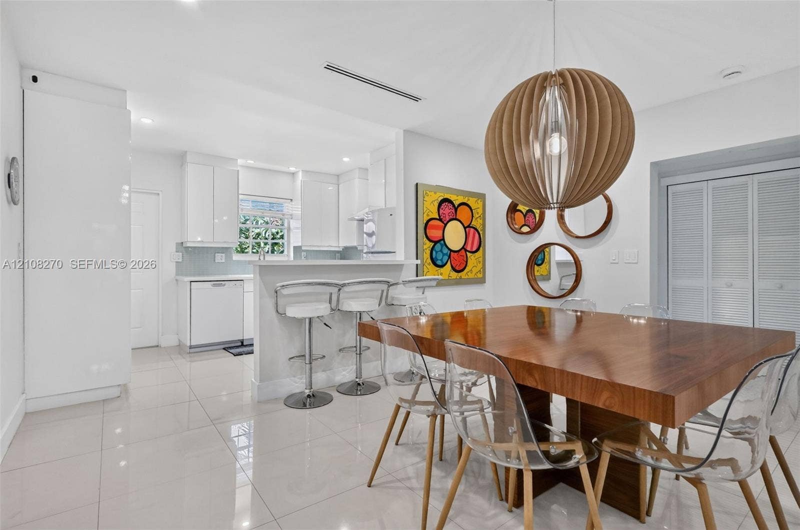 1125 99th Street, #12, Bay Harbor Islands, FL 33154 Kitchen featuring high-gloss cabinetry, stone-finish countertops, porcelain tile flooring, and a breakfast bar, complemented by a statement spherical wood-slat pendant light