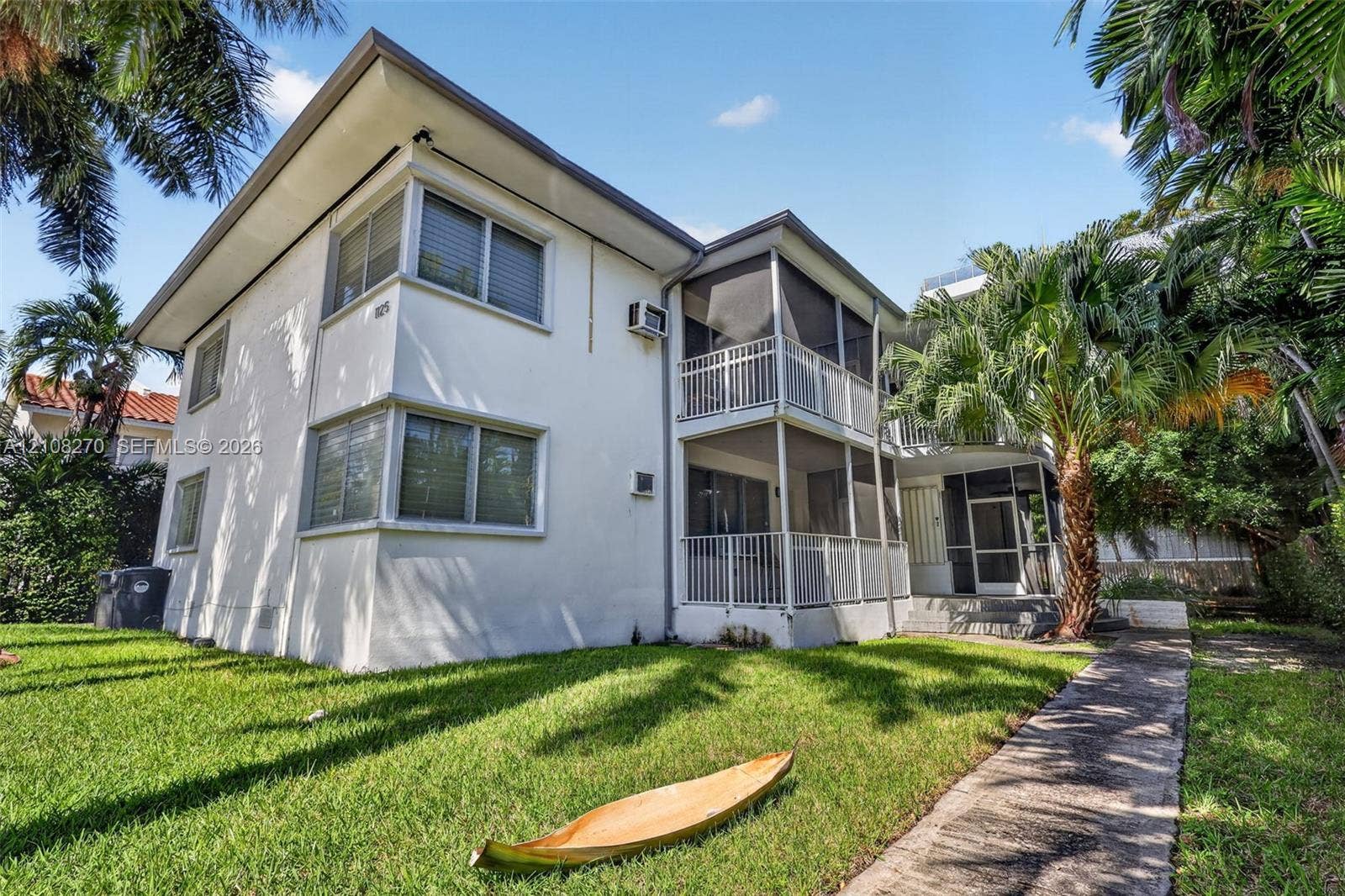 1125 99th Street, #12, Bay Harbor Islands, FL 33154 Two-story exterior featuring a white stucco facade, multi-level screened-in balconies with white metal railings, horizontal sliding windows, and a paved walkway