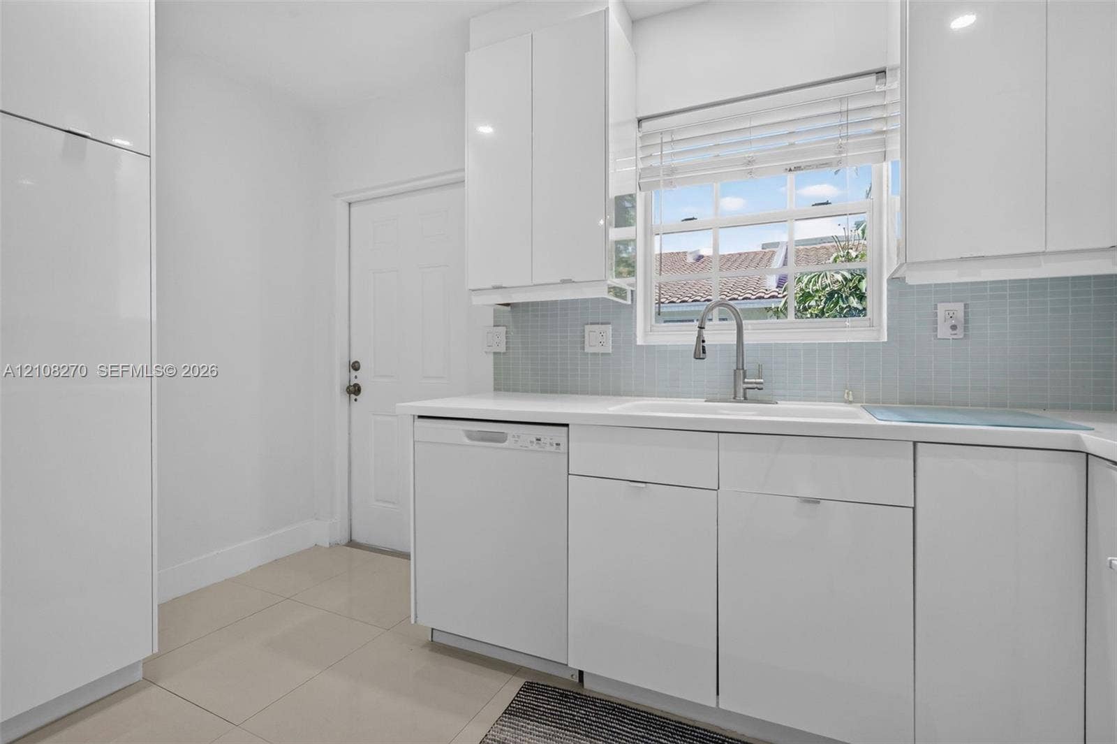 1125 99th Street, #12, Bay Harbor Islands, FL 33154 Kitchen featuring white high-gloss cabinetry, integrated dishwasher, light blue glass tile backsplash, white solid-surface countertops, and stainless steel gooseneck faucet