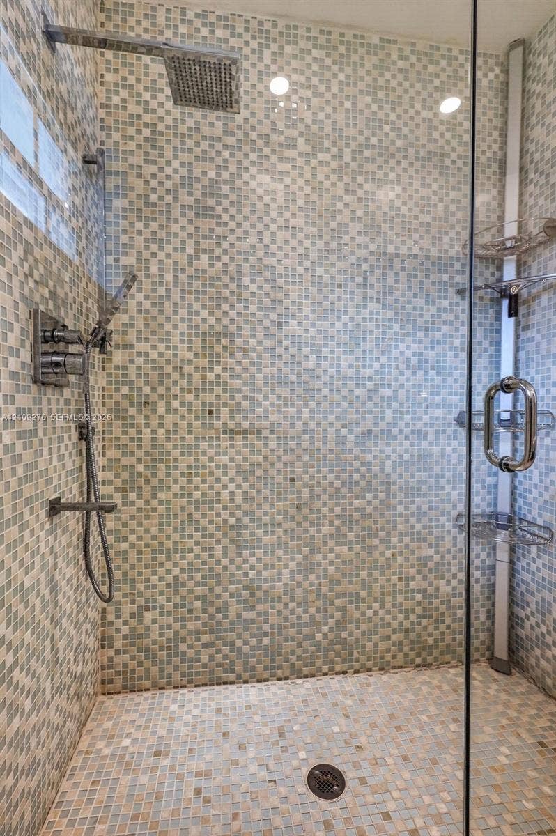 1125 99th Street, #12, Bay Harbor Islands, FL 33154 Walk-in shower featuring glass enclosure, mosaic tile wall surround, rainfall showerhead, handheld sprayer, and built-in corner shelving