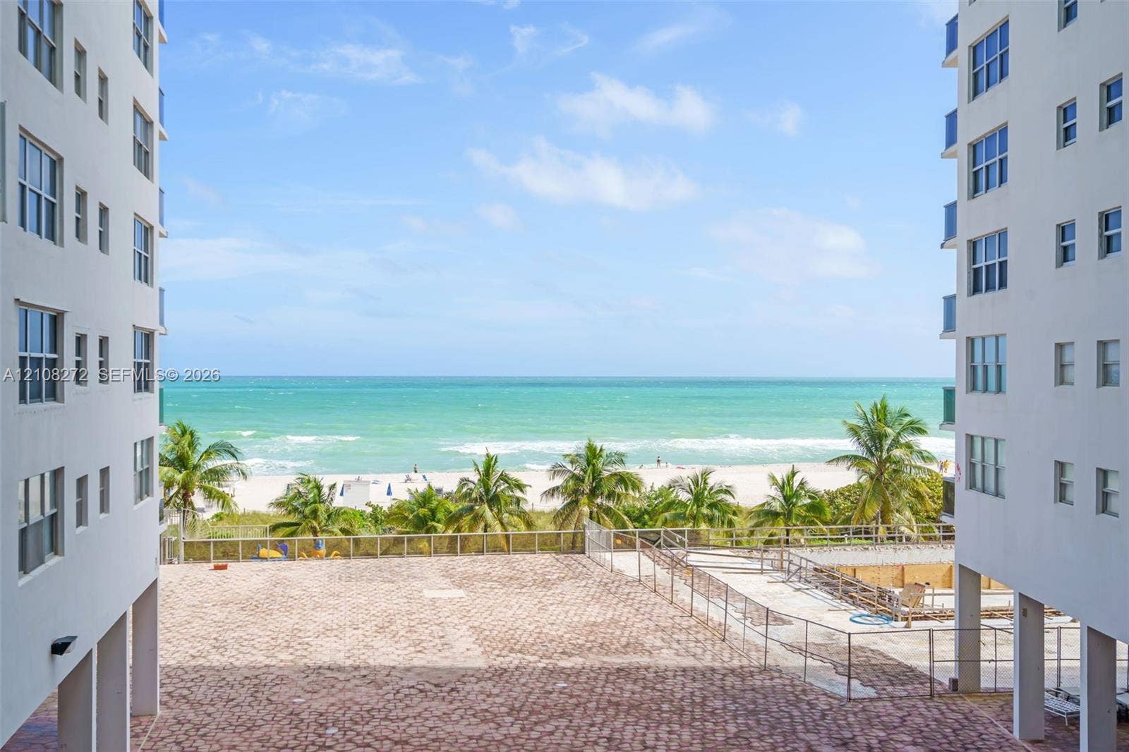 Paved plaza featuring perimeter metal fencing and direct oceanfront access to the sandy beach and coast
