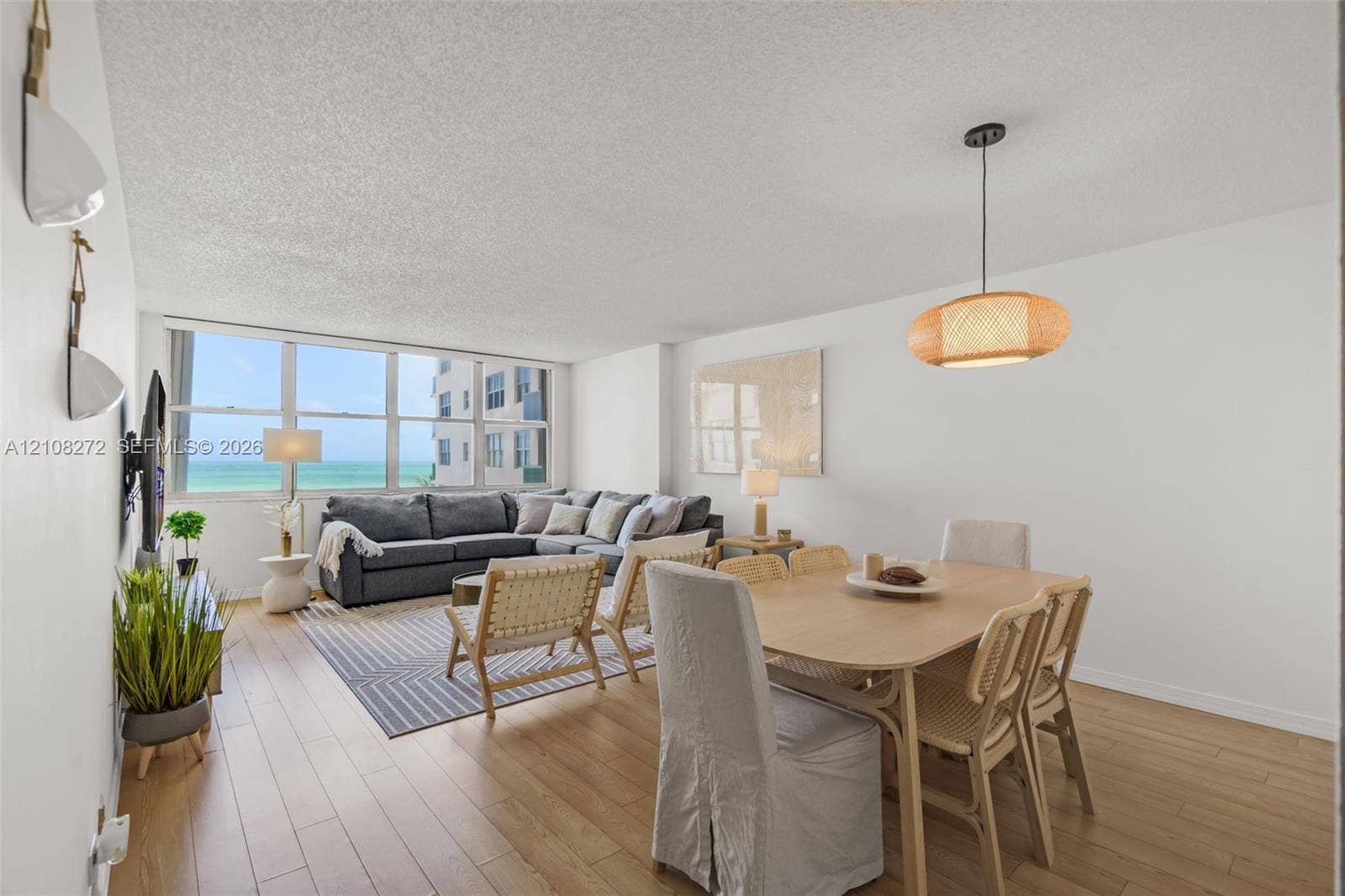 Open-concept floor plan featuring light wood-finish flooring, large floor-to-ceiling windows, and a woven pendant light fixture