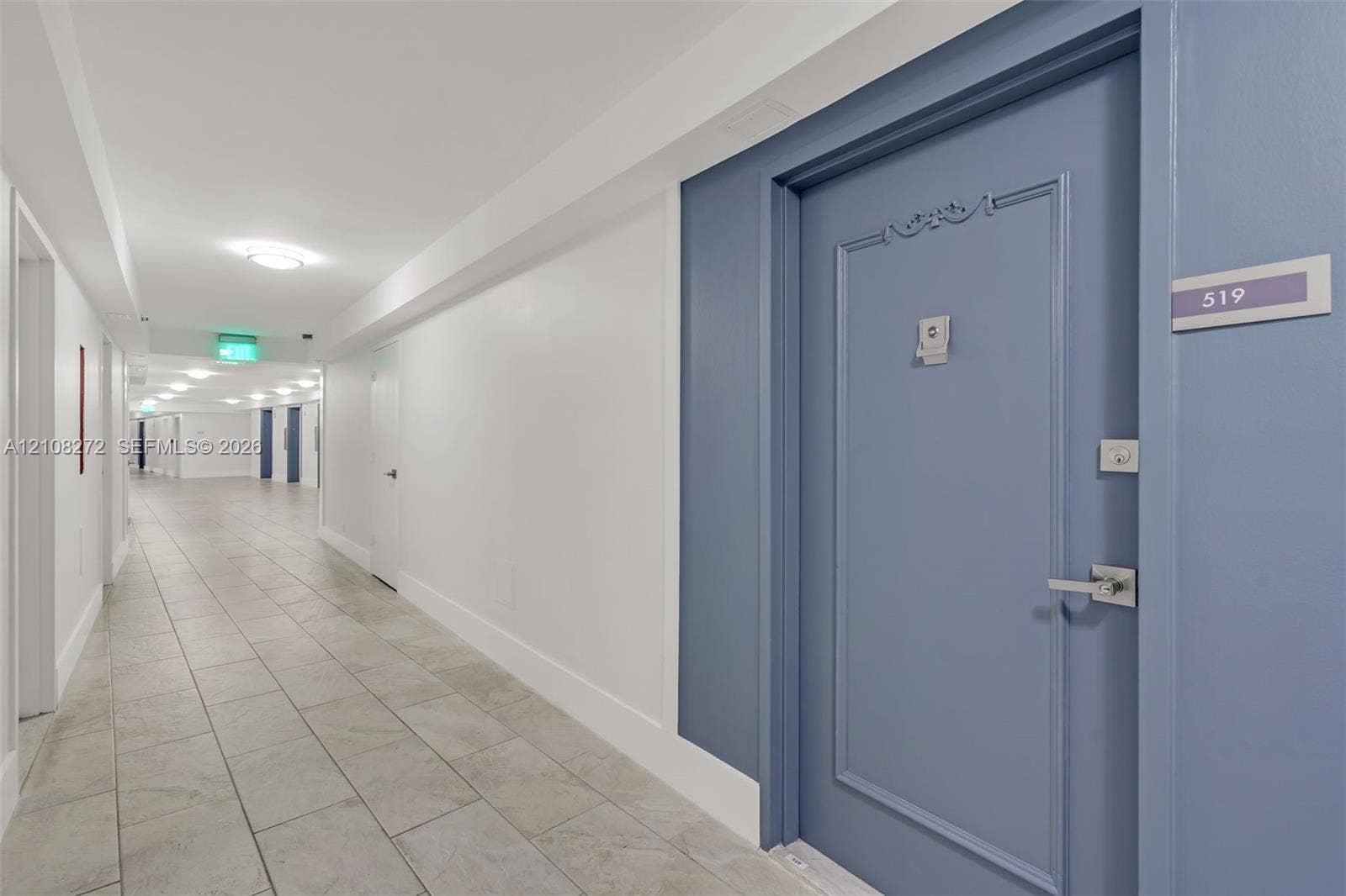 Blue paneled door with a metallic lever handle and ornate molding, polished porcelain-tile flooring, and recessed ceiling lighting