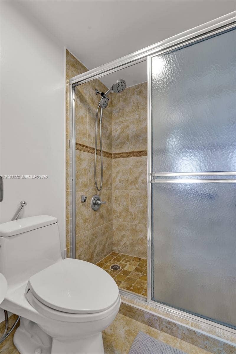 Shower enclosure featuring textured glass sliding doors, full-height stone-finish wall tiling with decorative inlay, and a multi-function showerhead with a handheld attachment