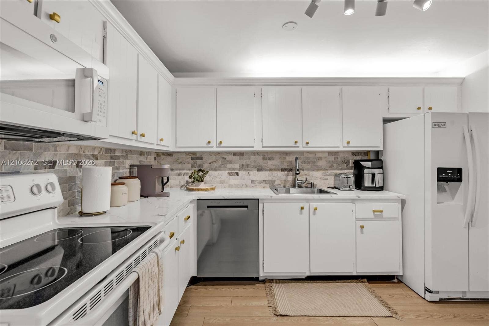 Kitchen featuring white shaker-style cabinetry, stone-patterned countertops, a multi-tonal stacked stone backsplash, stainless steel dishwasher, and wood-finish flooring