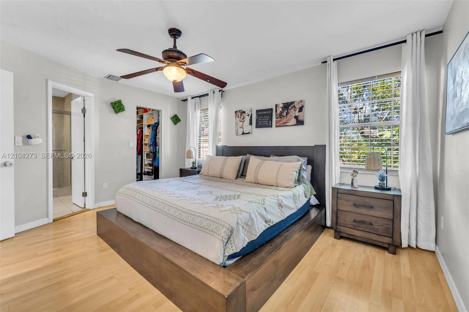 Bedroom featuring light wood-finish flooring, a ceiling fan with integrated lighting, and a walk-in closet with built-in organization