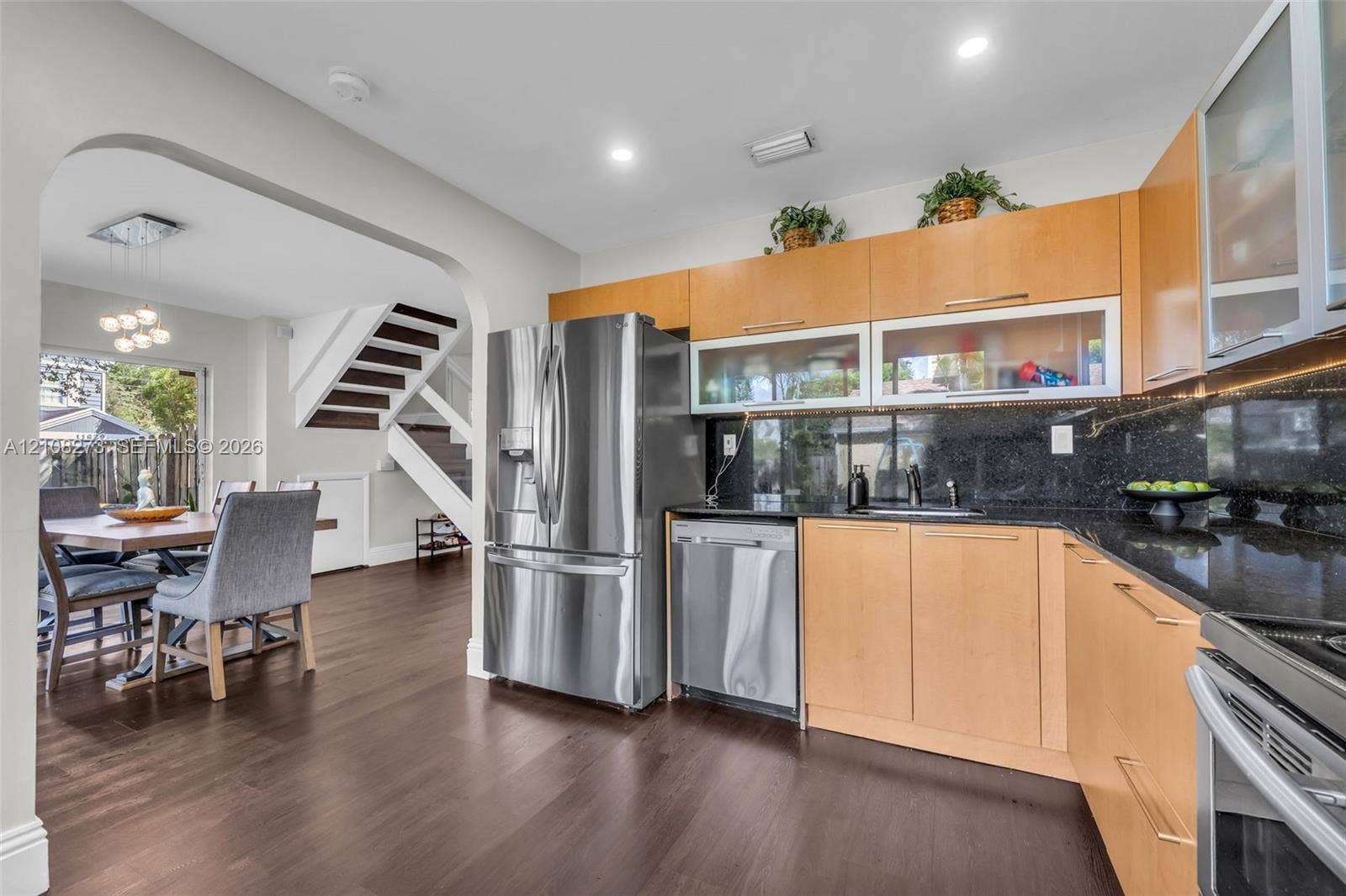 Kitchen featuring light wood-finish cabinetry, dark stone countertops, stainless steel appliances, and dark wood-finish flooring