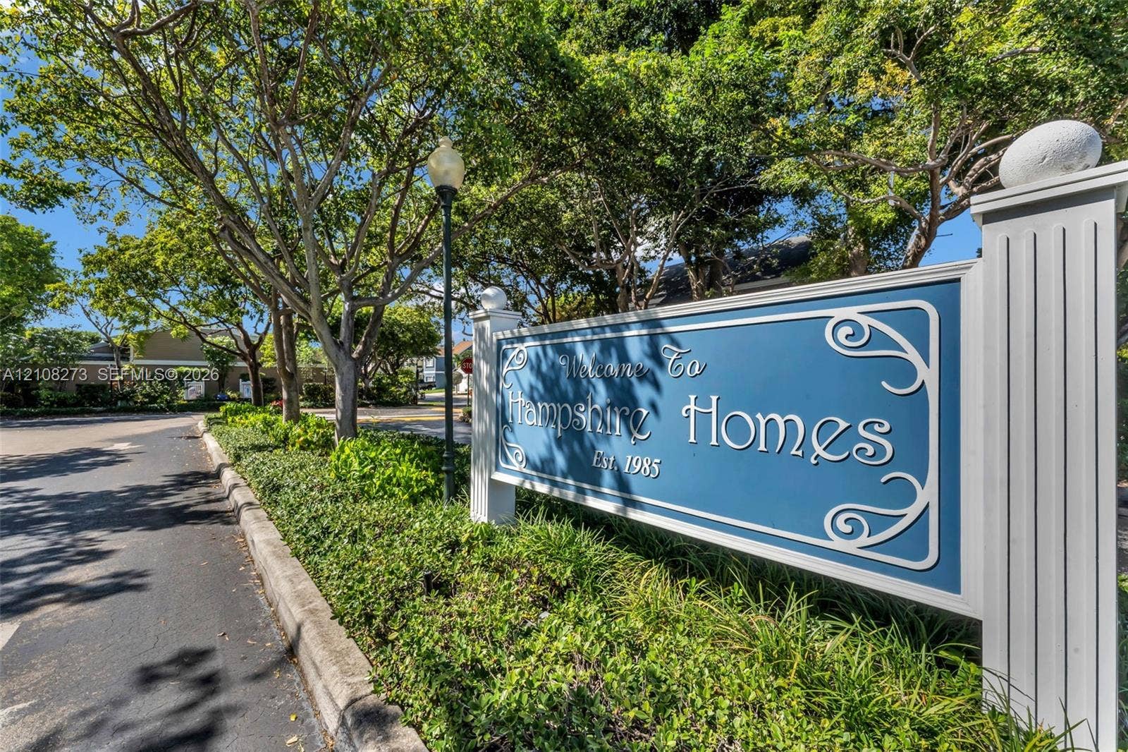 Community entrance signage featuring architectural column detailing, integrated landscaping, and mature canopy trees