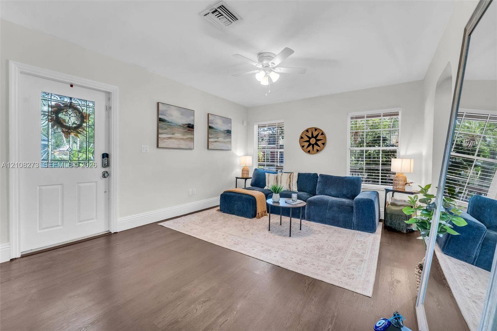 Wood-finish flooring, white entry door with decorative glass panel, ceiling fan with integrated light fixture, and dual windows