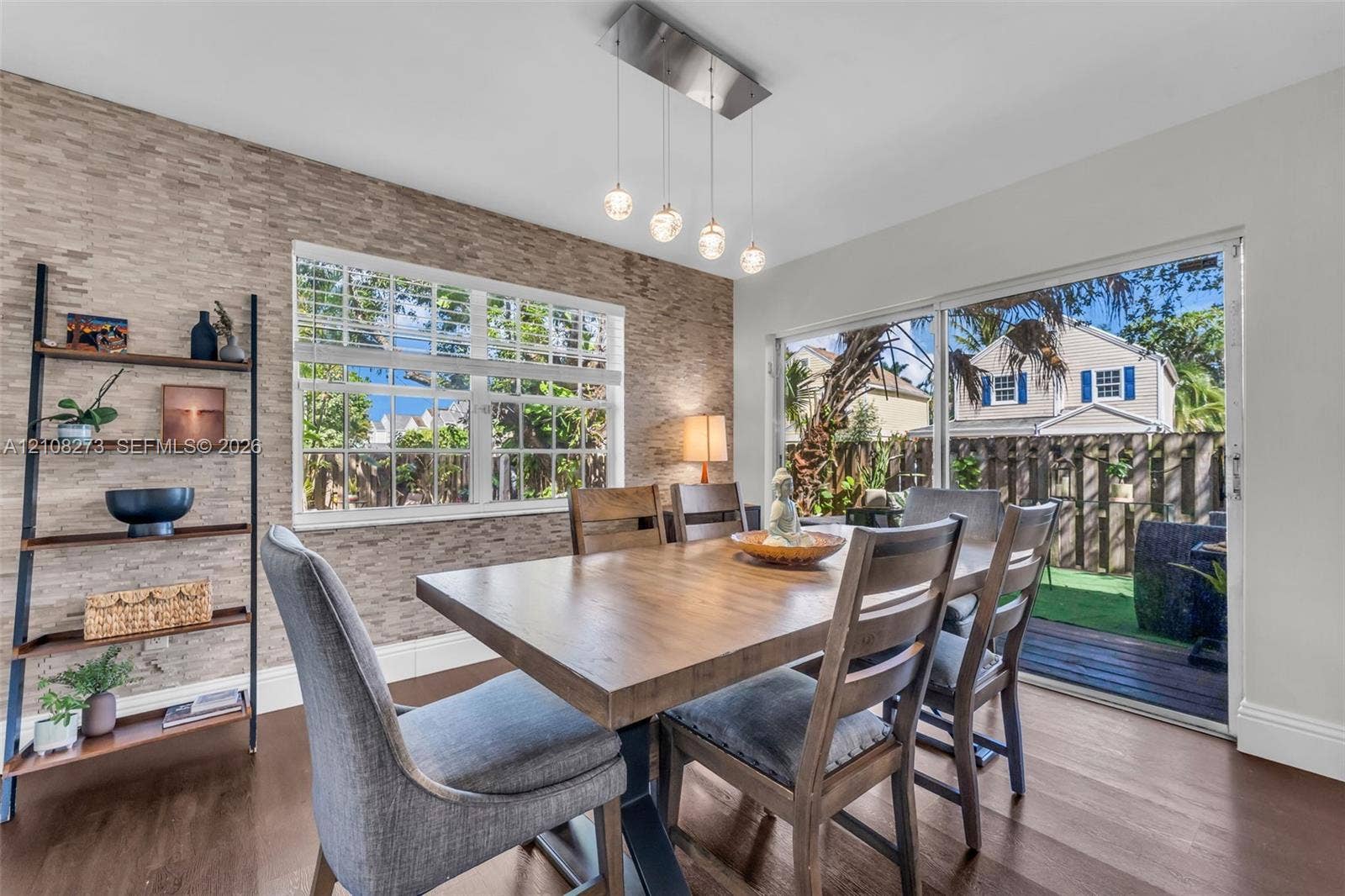Textured stone accent wall, multi-light pendant fixture, grid-patterned windows, wood-finish flooring, and sliding glass doors