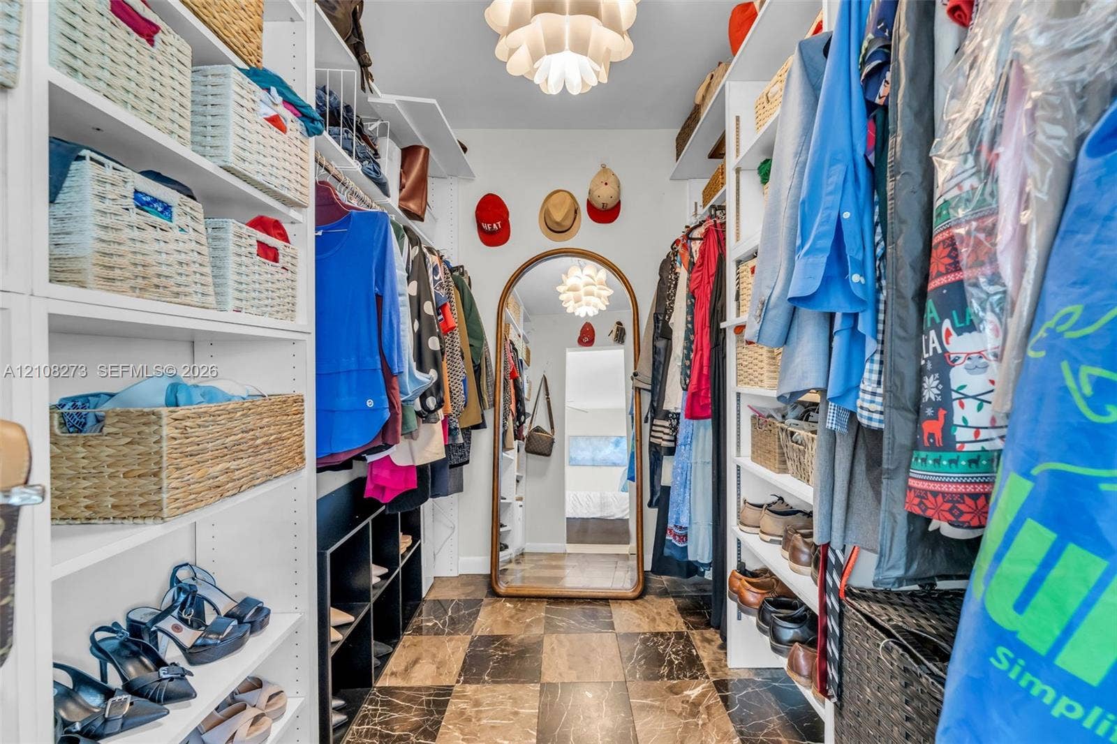 Custom walk-in closet featuring white built-in shelving, checkered stone-tile flooring, and a decorative ceiling fixture