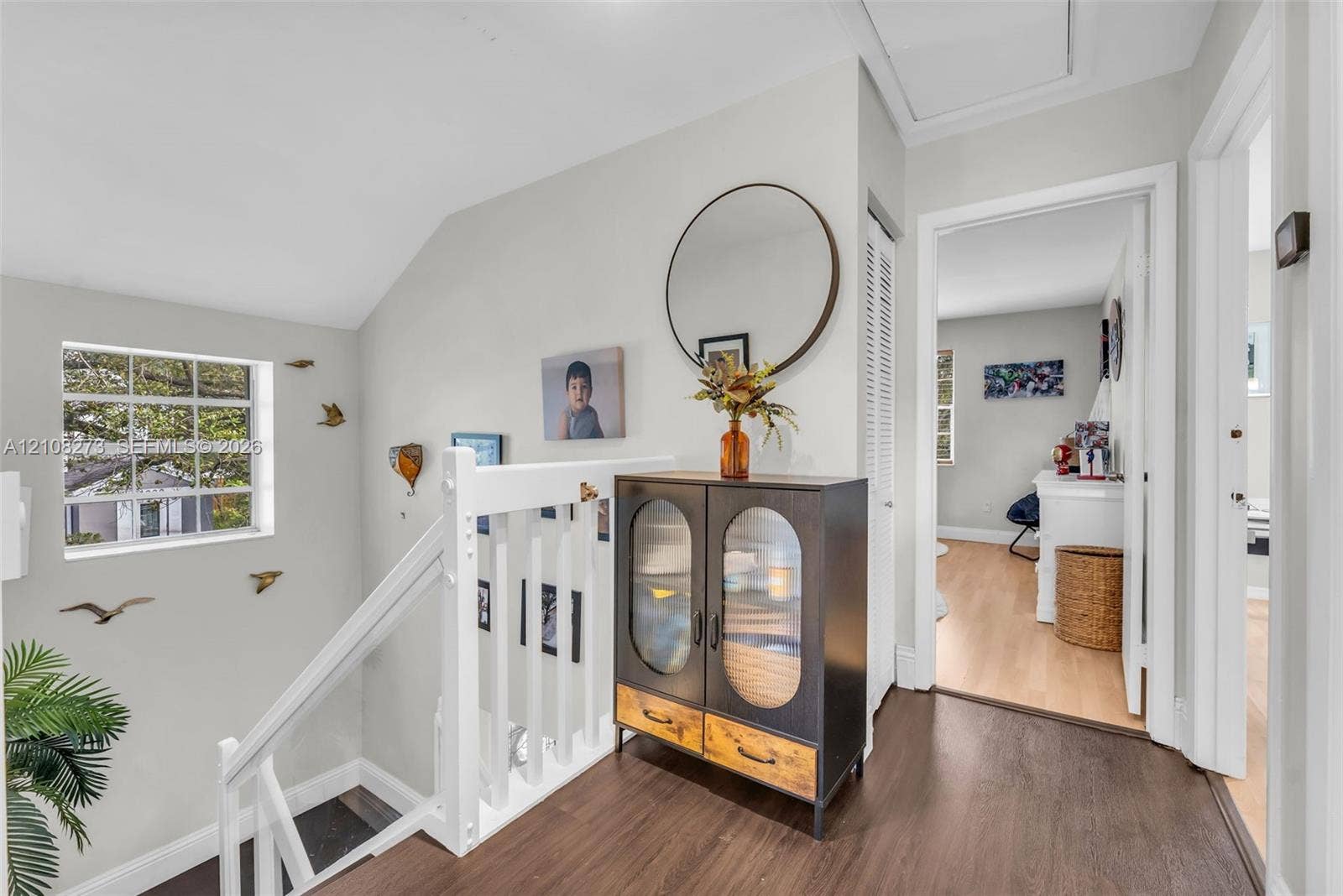 White wooden railing with balusters, wood-finish flooring, multi-pane window, and louvered closet door