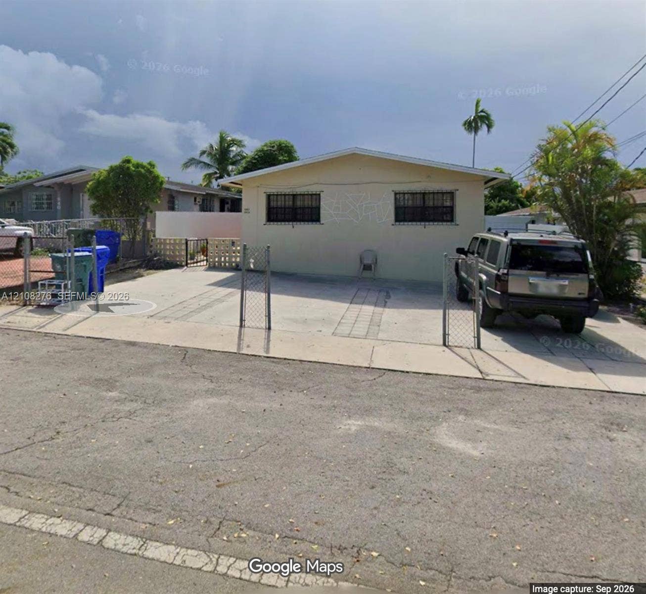Single-story residence featuring a concrete driveway, metal chain-link perimeter fencing, and exterior window security bars