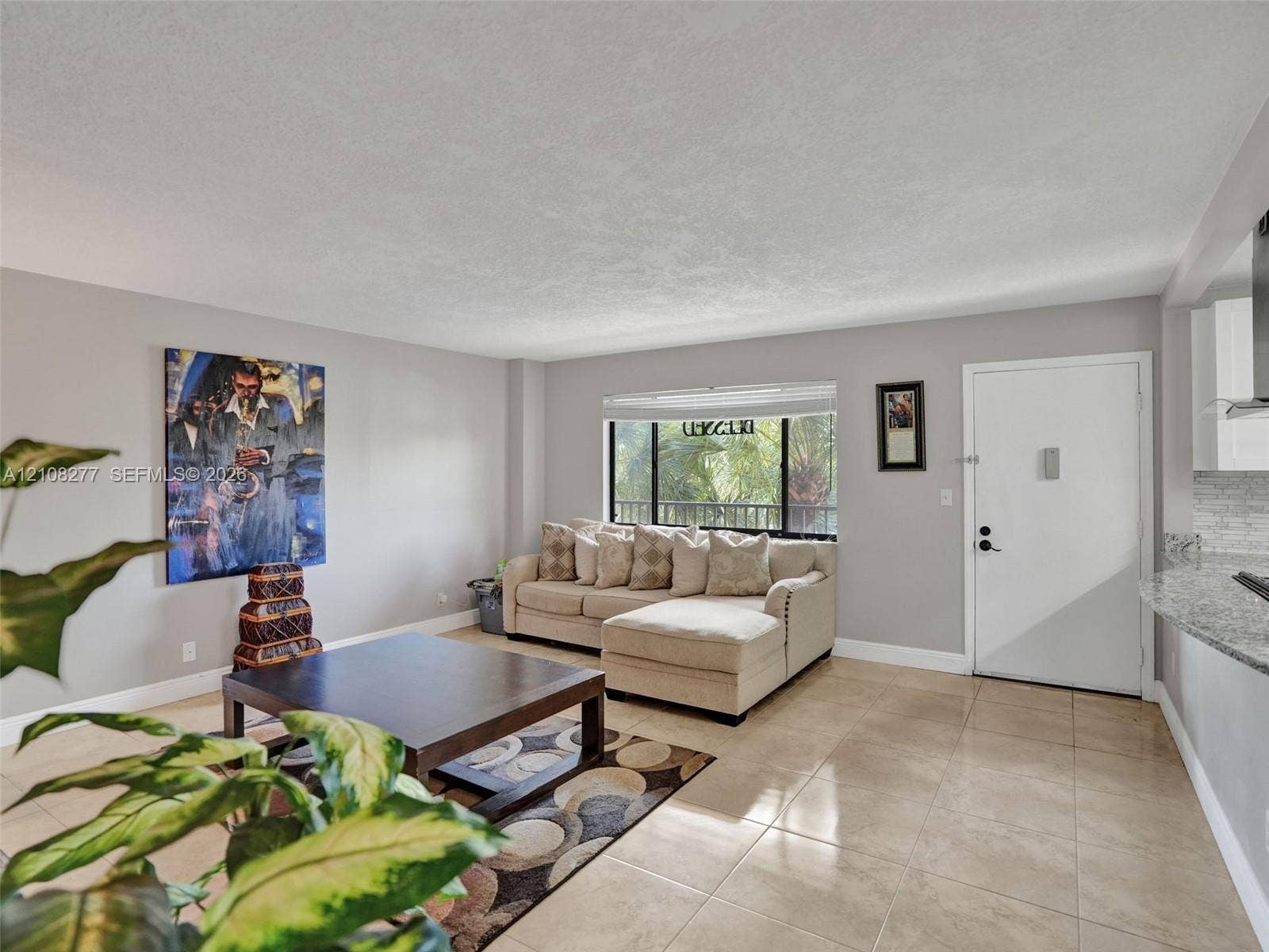 7466 Ashmont Circle, #303, Tamarac, FL 33321 Open-concept interior featuring neutral wall tones, large-format tile flooring, a wide window with blinds, and a stone-surface kitchen counter