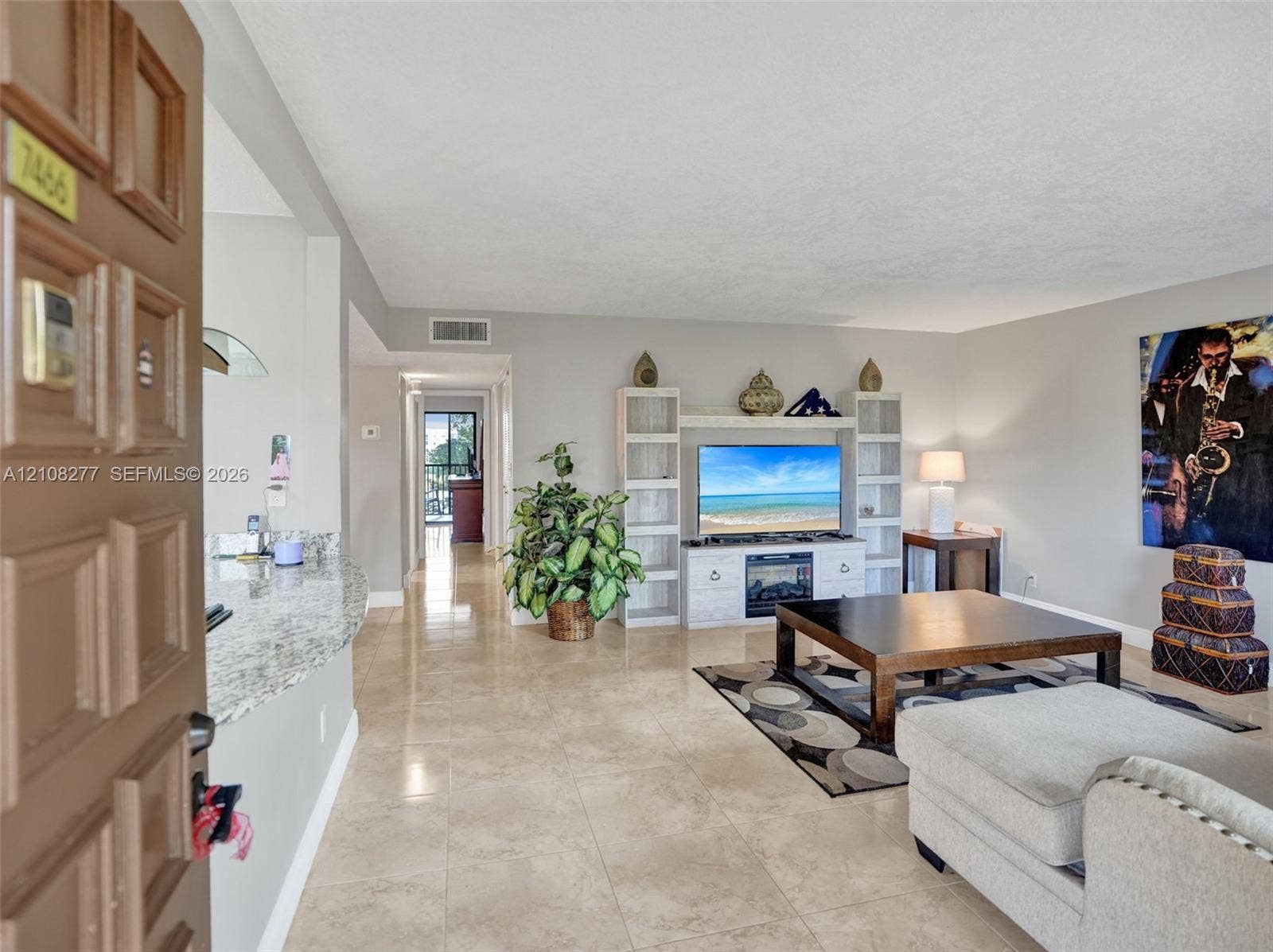 7466 Ashmont Circle, #303, Tamarac, FL 33321 Open-concept interior featuring neutral stone-finish tile flooring, a stone-surfaced breakfast bar, and a built-in media center with integrated fireplace