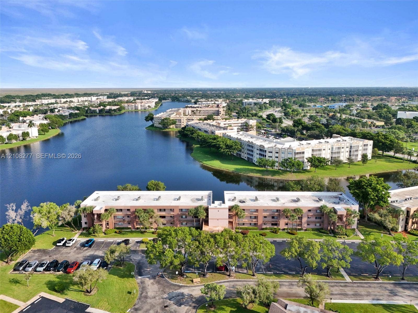 7466 Ashmont Circle, #303, Tamarac, FL 33321 Aerial perspective of a multi-story residential building featuring exterior masonry cladding, paved parking areas, and mature landscaping situated on a waterfront lot