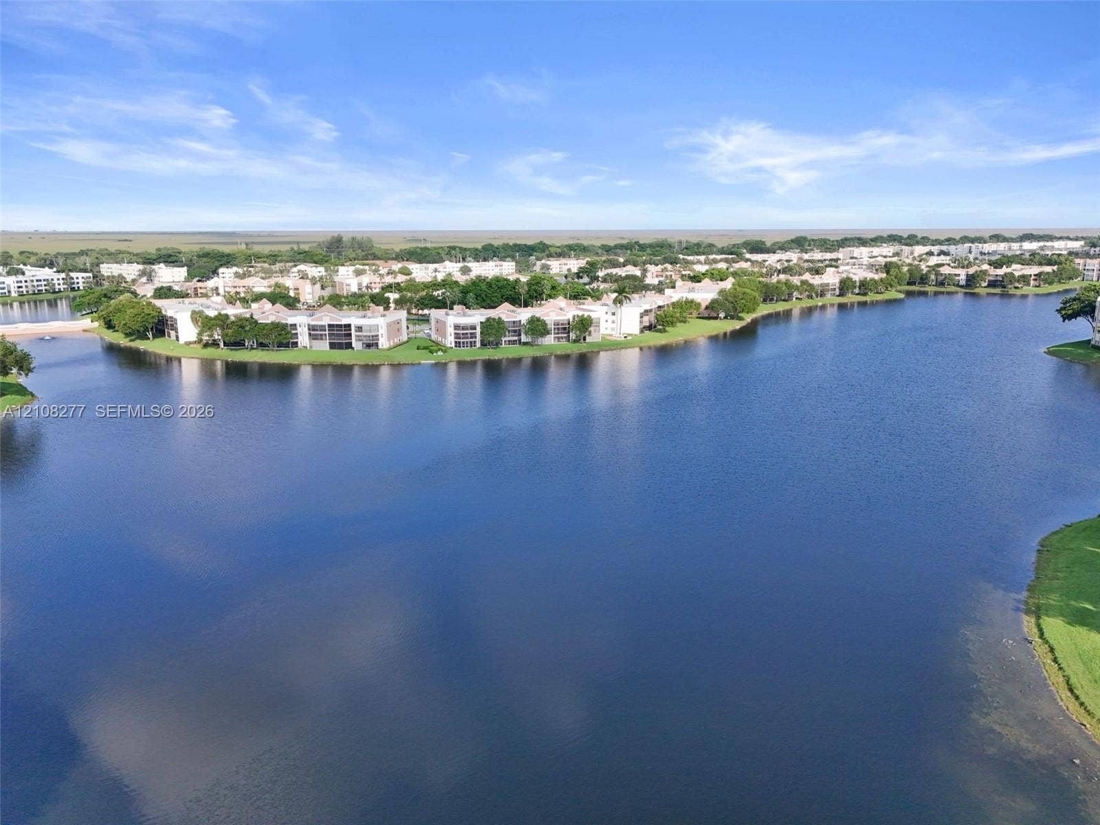 7466 Ashmont Circle, #303, Tamarac, FL 33321 Aerial perspective of multi-unit residential structures situated along a large body of water, featuring expansive water frontage and mature landscaping