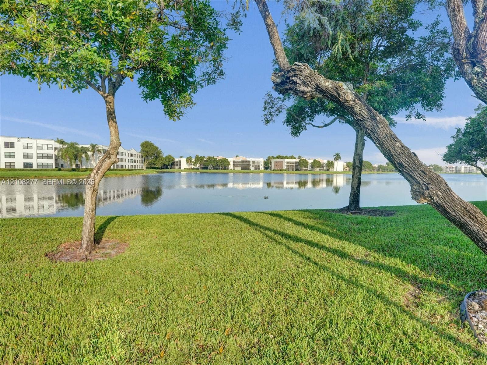7466 Ashmont Circle, #303, Tamarac, FL 33321 Waterfront lot featuring a manicured lawn, mature trees, and direct water access