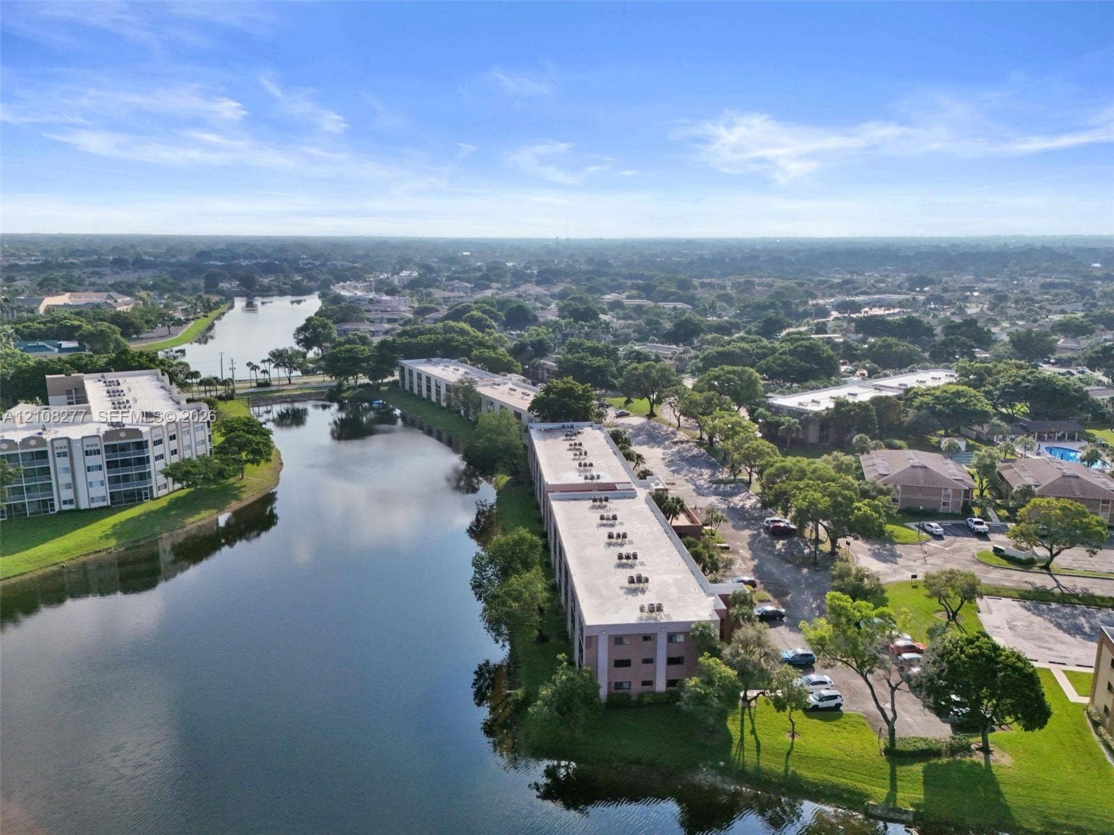7466 Ashmont Circle, #303, Tamarac, FL 33321 Aerial perspective of waterfront multi-story buildings featuring paved parking, manicured landscaping, and mature trees