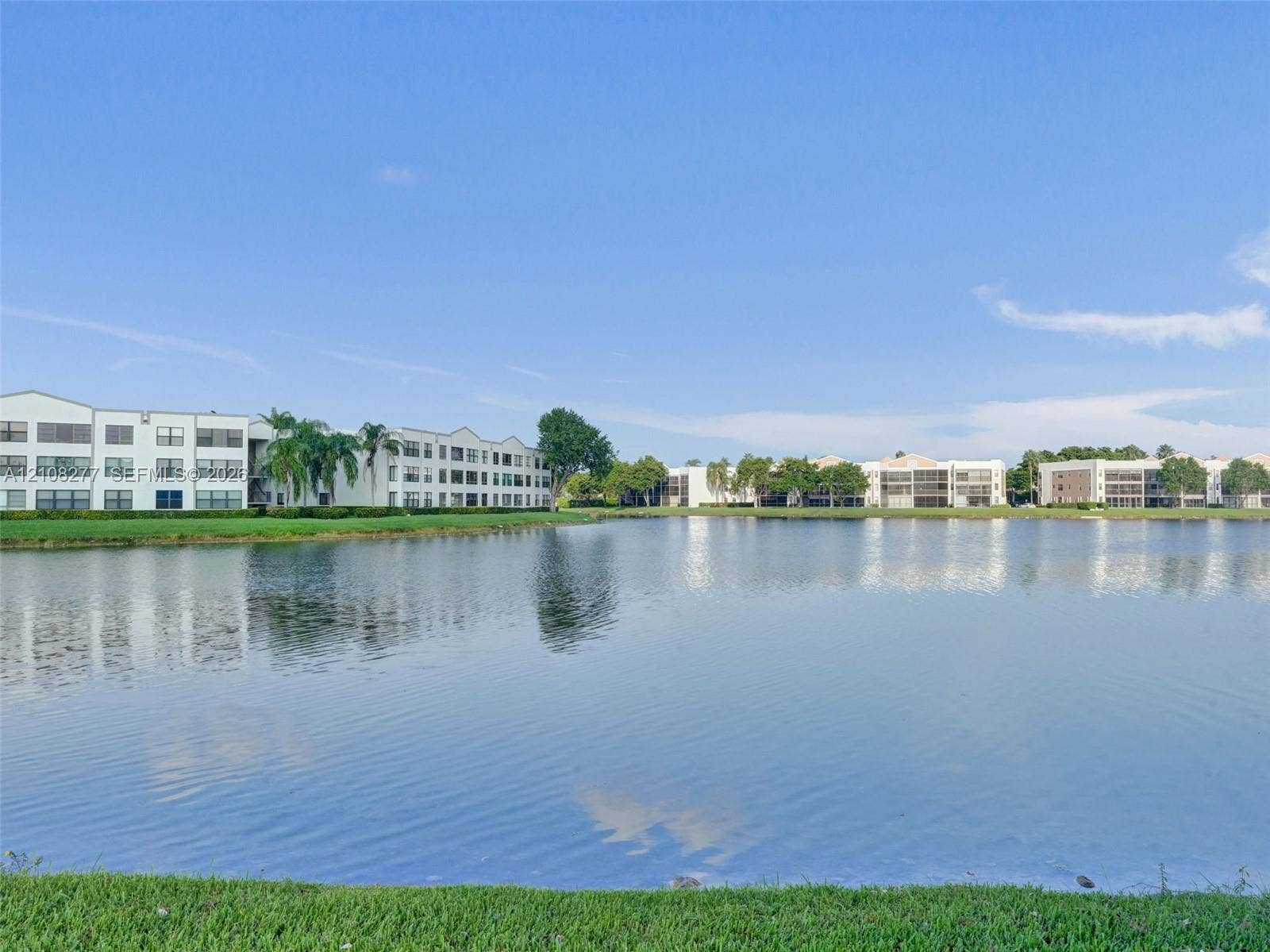 7466 Ashmont Circle, #303, Tamarac, FL 33321 Waterfront setting featuring a multi-story exterior with stucco finish and a manicured grass perimeter