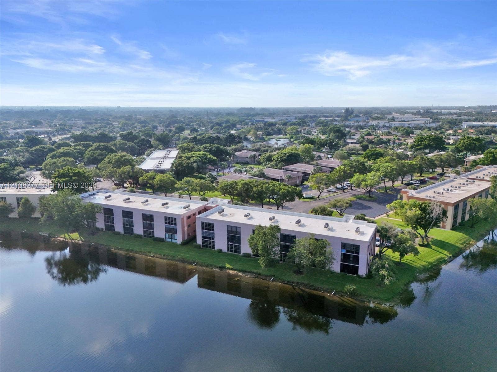 7466 Ashmont Circle, #303, Tamarac, FL 33321 Waterfront multi-story residential building featuring exterior balconies, flat roofline, and landscaped perimeter grounds