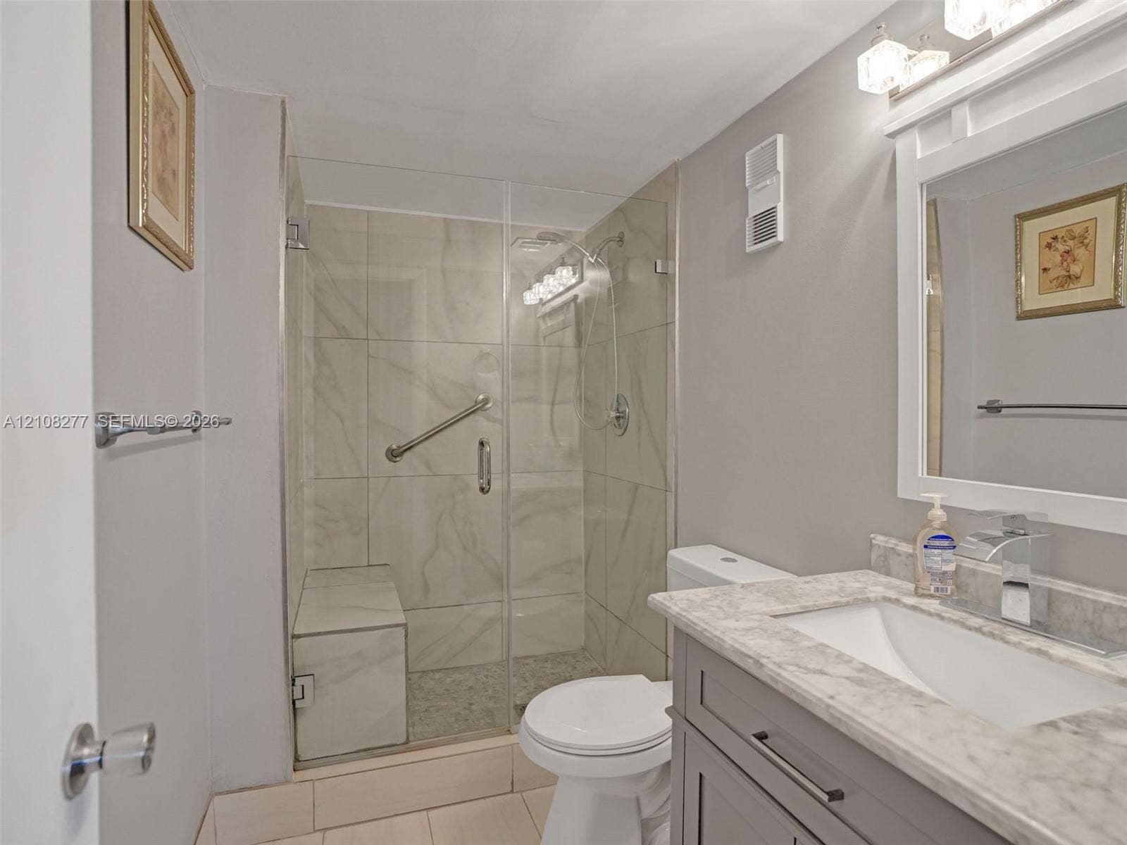 7466 Ashmont Circle, #303, Tamarac, FL 33321 Bathroom featuring a walk-in shower with glass enclosure, built-in tiled bench, stone-finish countertop, vanity with shaker-style cabinetry, and wall-mounted light fixture