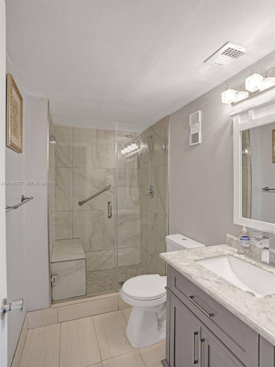 7466 Ashmont Circle, #303, Tamarac, FL 33321 Bathroom featuring a dark-finish vanity with a stone-top integrated sink, glass-enclosed shower with tile surround and built-in bench, and polished chrome fixtures