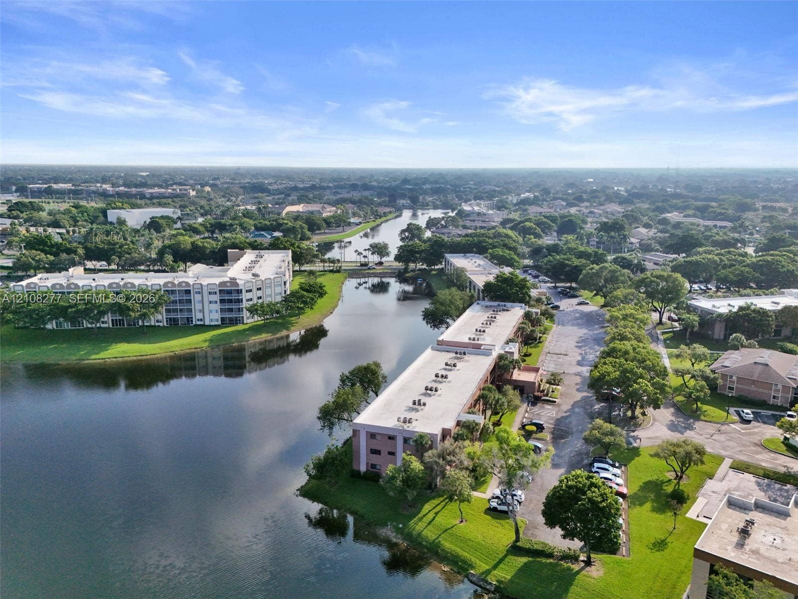7466 Ashmont Circle, #303, Tamarac, FL 33321 Aerial perspective featuring waterfront residential buildings, mature trees, and landscaped green space