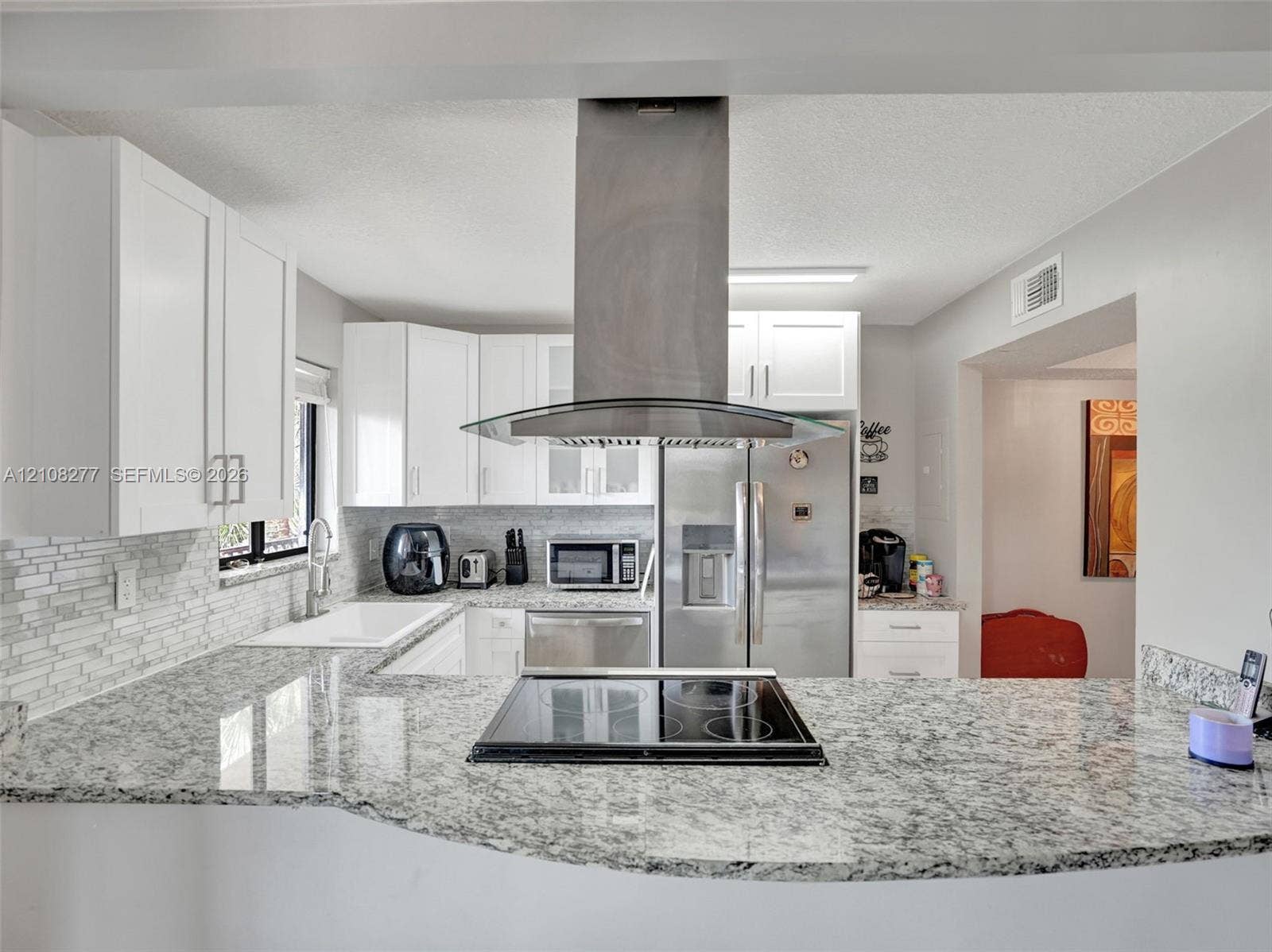 7466 Ashmont Circle, #303, Tamarac, FL 33321 Kitchen featuring stone-finish countertops, stainless steel chimney-style range hood, electric cooktop, white cabinetry, and a subway tile backsplash