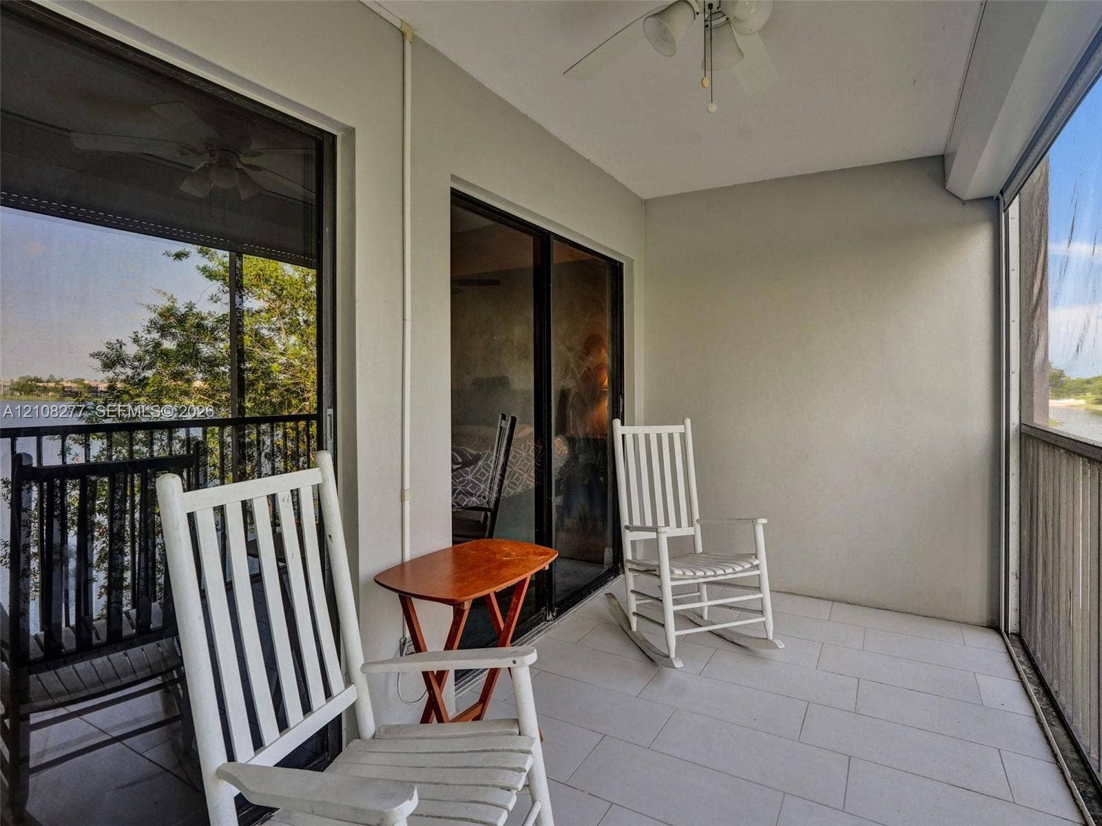 7466 Ashmont Circle, #303, Tamarac, FL 33321 Covered balcony featuring neutral tile flooring, dual sliding glass door access, a mounted ceiling fan, and screened enclosures